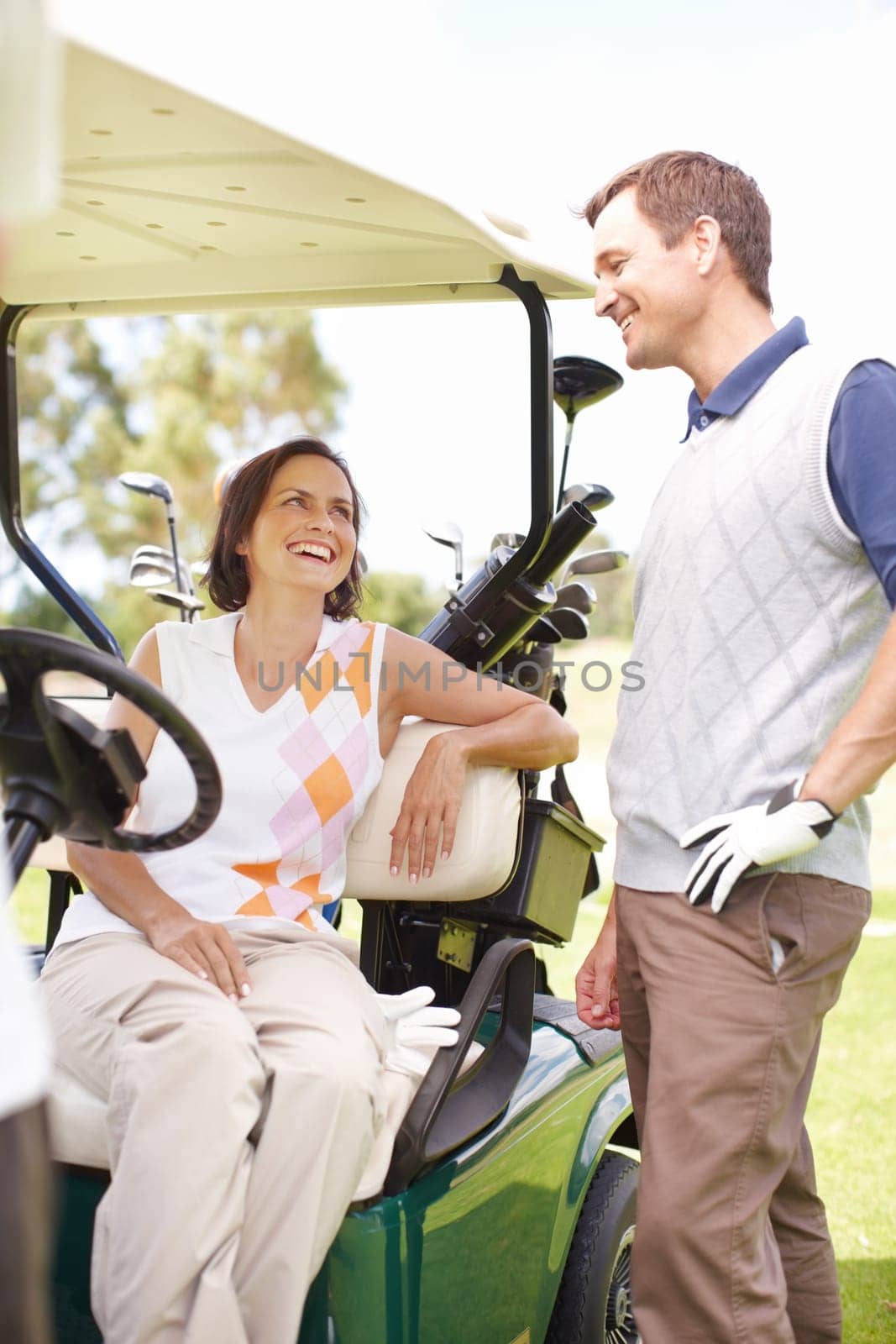 Taking a moment to relax between holes. Smiling woman seated in a golf cart with her husband standing alongside her