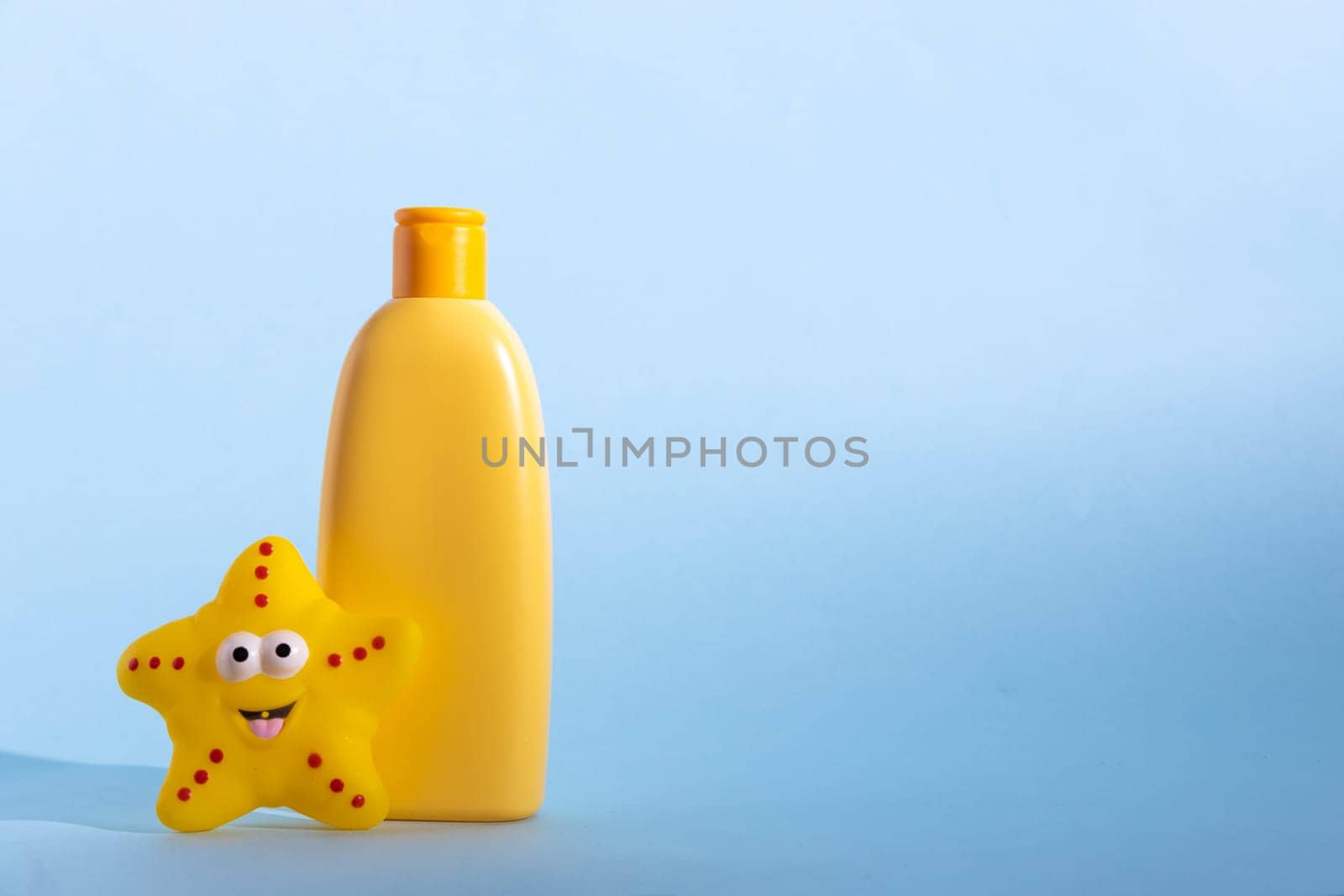 Yellow plastic bottle with baby cosmetic and funny bath toy. The concept of kid's skin care