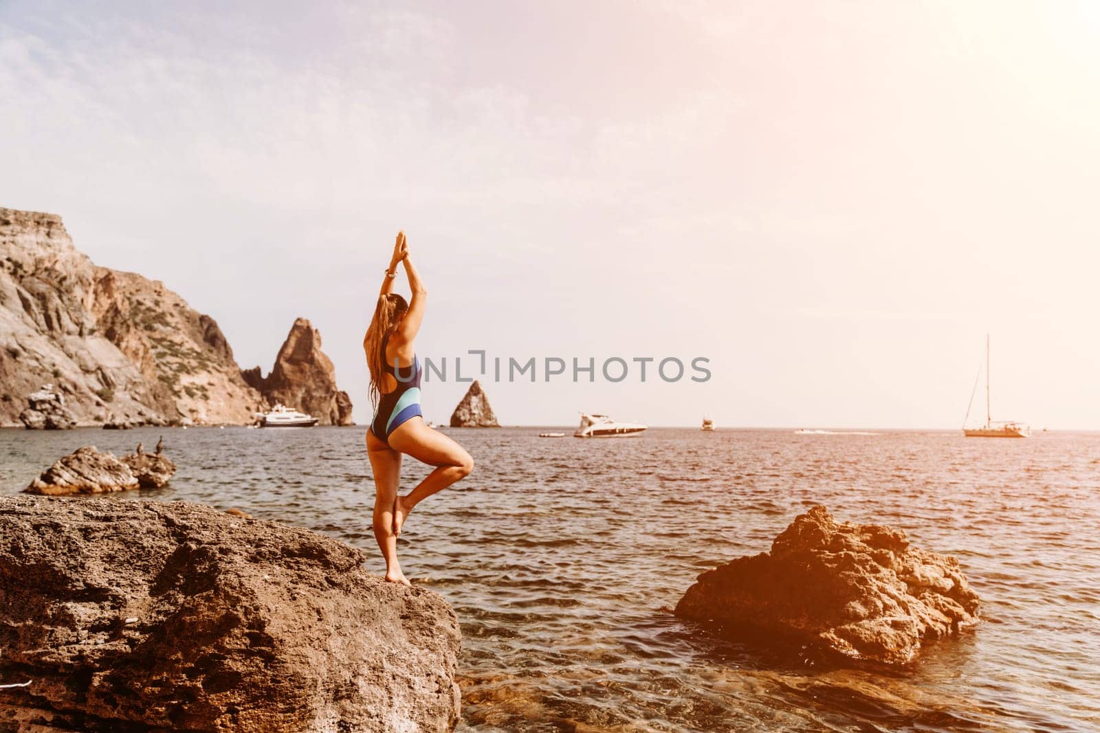 Yoga on the beach. A happy woman meditating in a yoga pose on the beach, surrounded by the ocean and rock mountains, promoting a healthy lifestyle outdoors in nature, and inspiring fitness concept