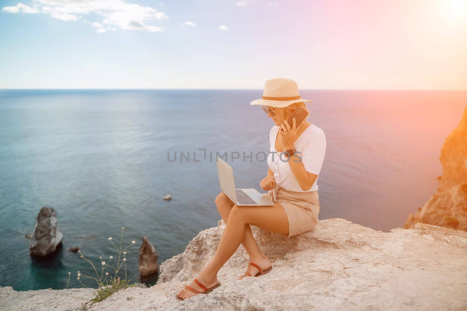 Freelance women sea. She is working on the computer, talking on the phone in the open air with a beautiful view of the sea. The concept of remote work