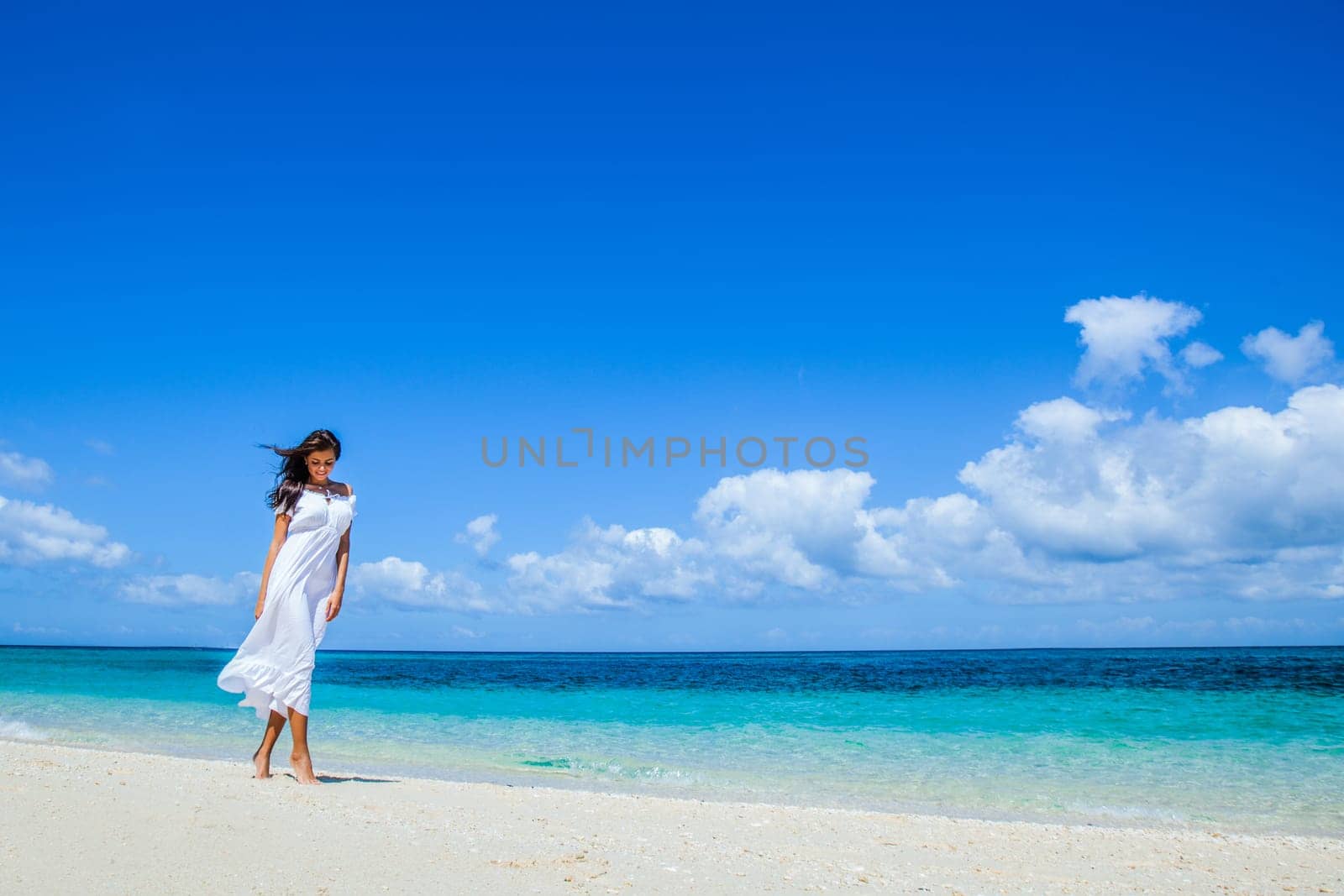 Young woman in white dress walking along sand tropical beach