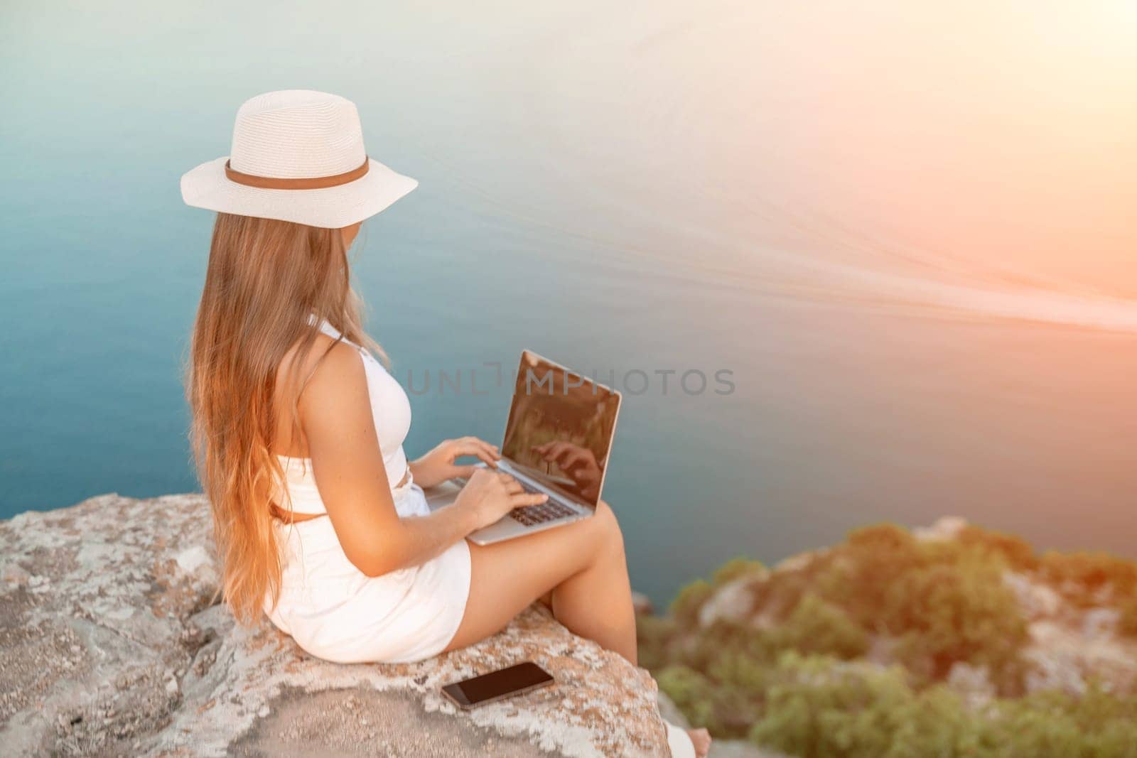 Freelance women sea working on the computer. Good looking middle aged woman typing on a laptop keyboard outdoors with a beautiful sea view. The concept of remote work