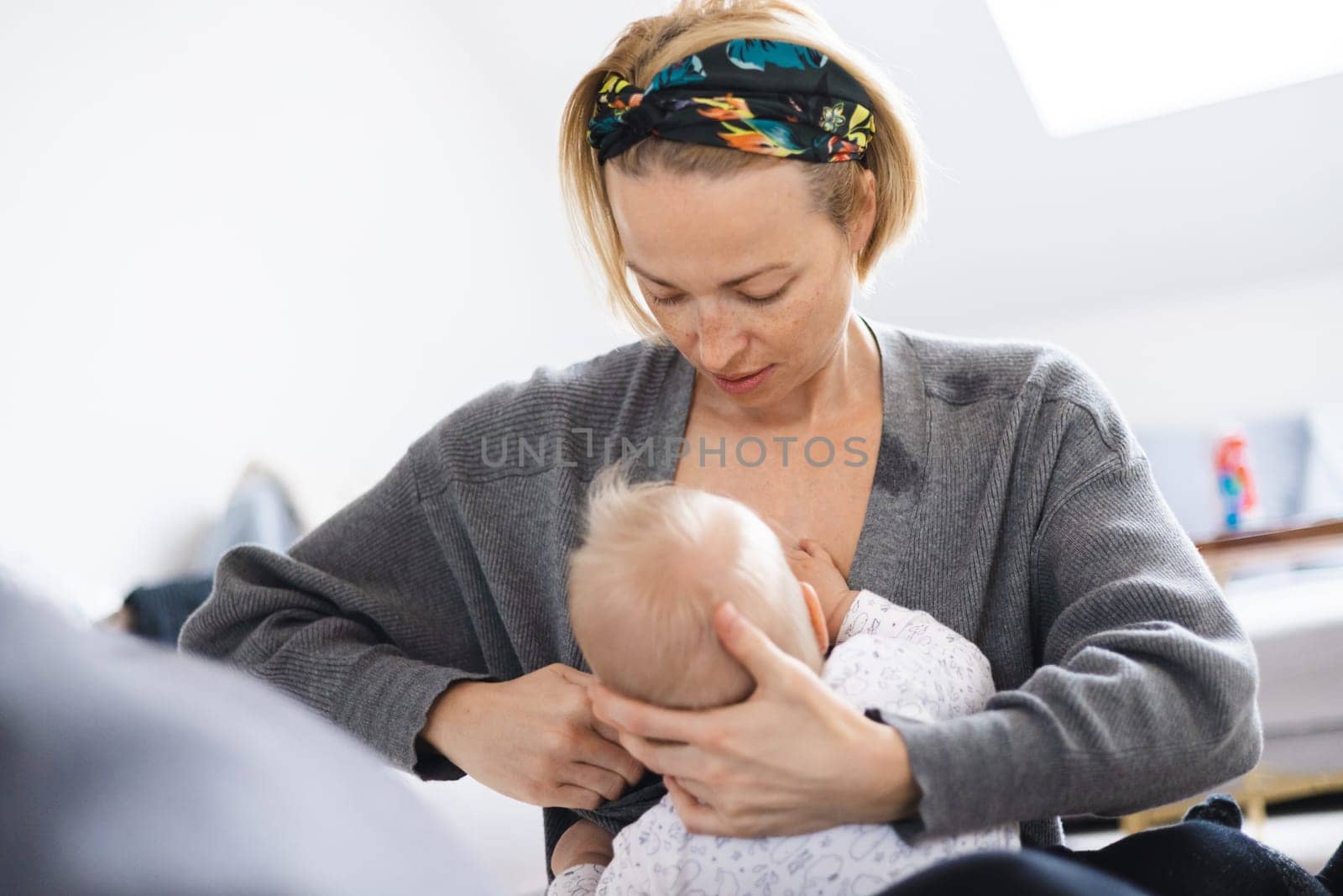 Young woman breastfeeding her infant baby boy casualy sitting on child's playing mat on living room floor at home