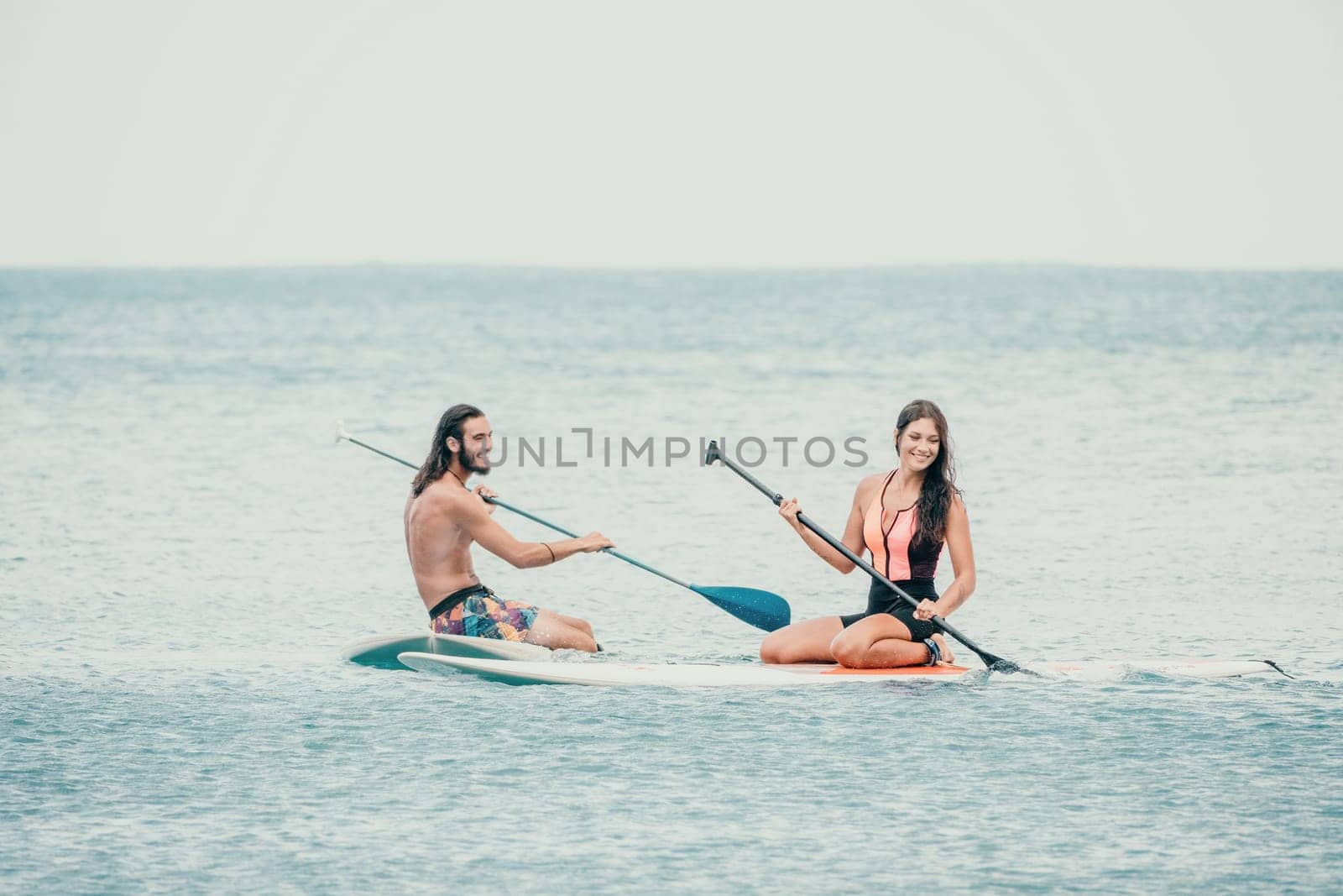 Sea woman and man on sup. Silhouette of happy young woman and man, surfing on SUP board, confident paddling through water surface. Idyllic sunset. Active lifestyle at sea or river