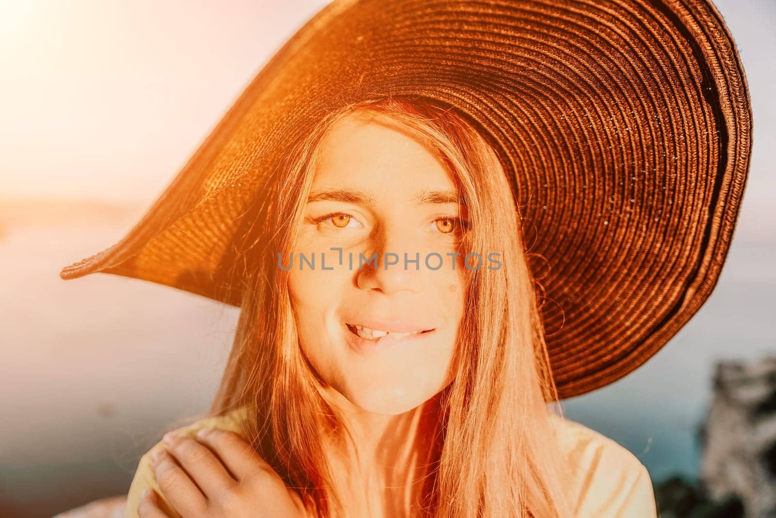 Portrait of happy young woman wearing summer black hat with large brim at beach on sunset. Closeup face of attractive girl with black straw hat. Happy young woman smiling and looking at camera at sea. by panophotograph
