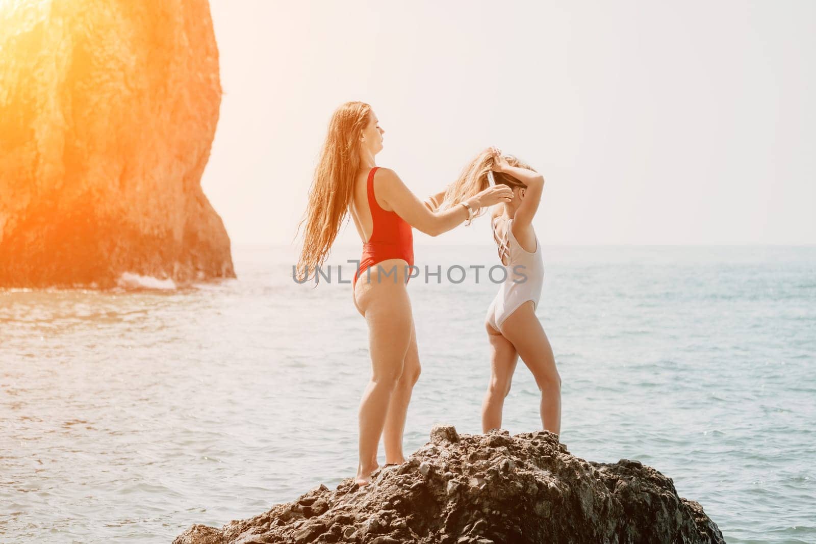 Woman and her daughter together on rock in the sea. Silhouette mother and daughter doing yoga at beach by panophotograph