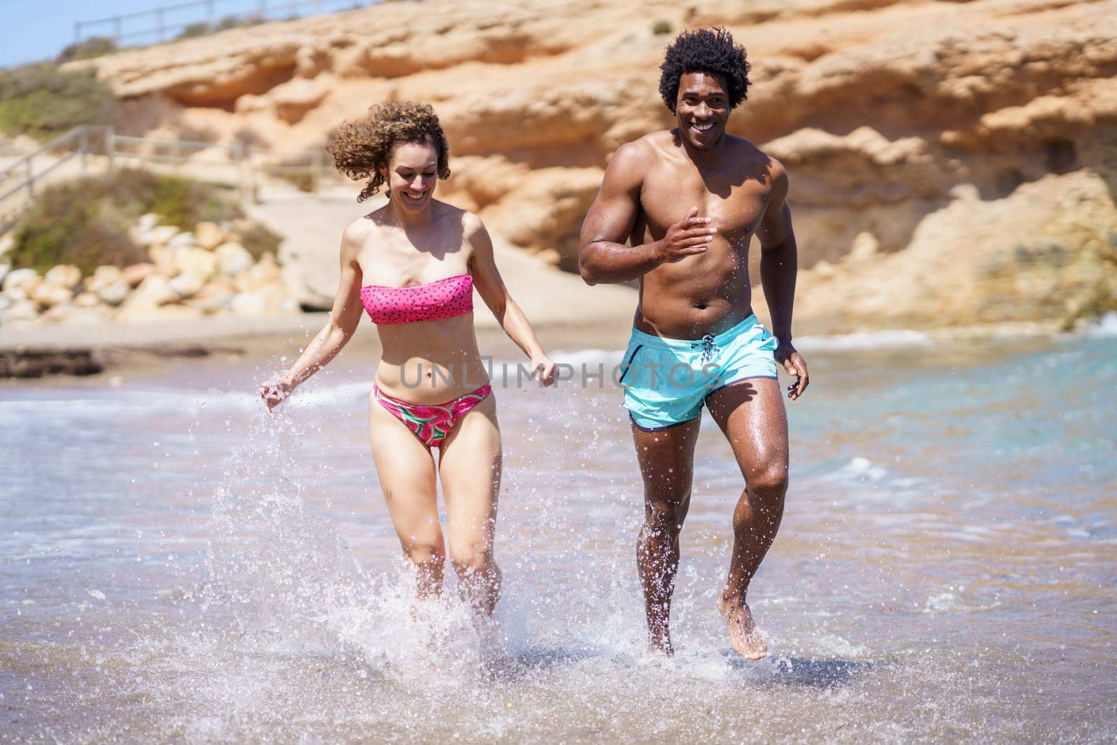 Happy multiracial couple sprinting in seawater in sunlight by javiindy