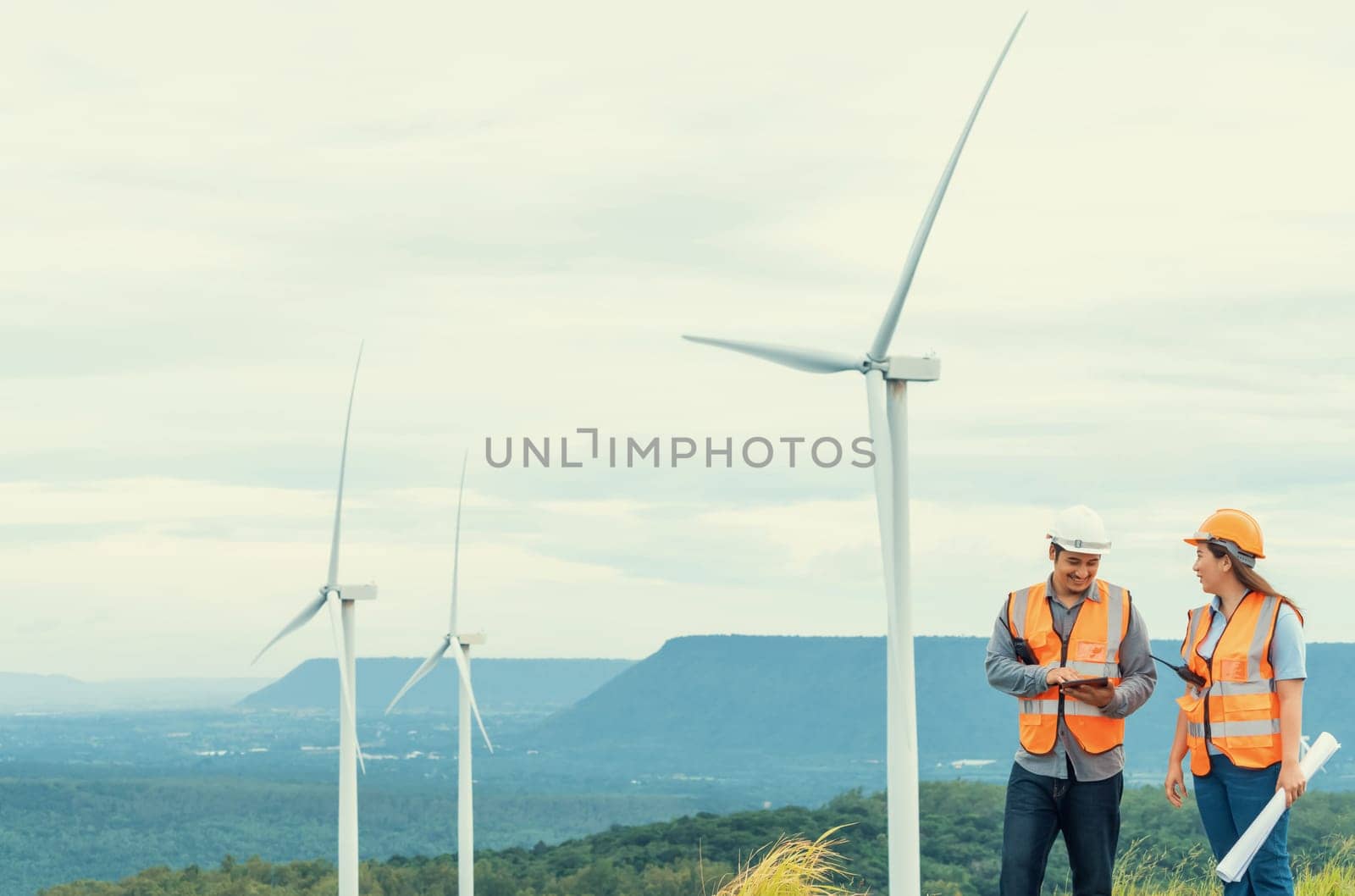 Male and female engineers working on a wind farm atop a hill or mountain in the rural. Progressive ideal for the future production of renewable, sustainable energy.