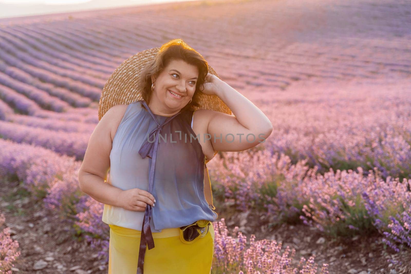 Woman lavender field sunset. Romantic woman walks through the lavender fields. illuminated by sunset sunlight. Dressed in a dress with a hat