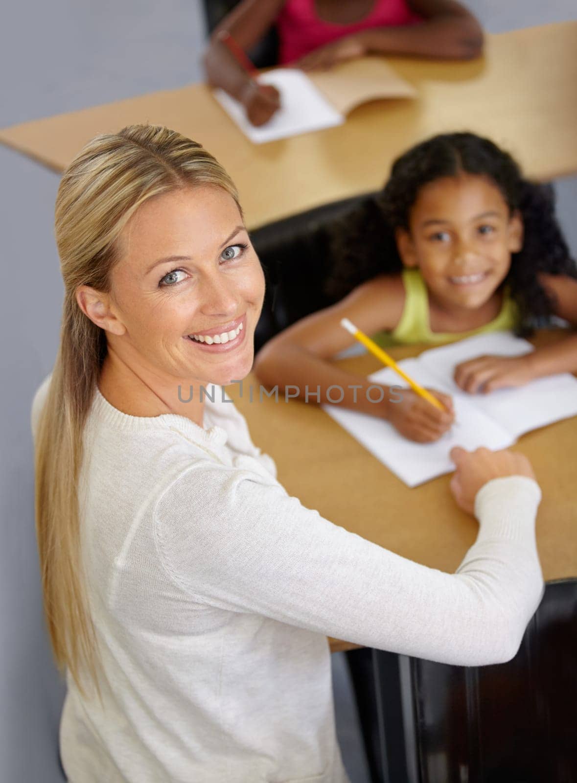 Kid, teacher and portrait in classroom studying school work for an education with support. Woman, smile and desk with child to help with reading or learning for children to work at school building