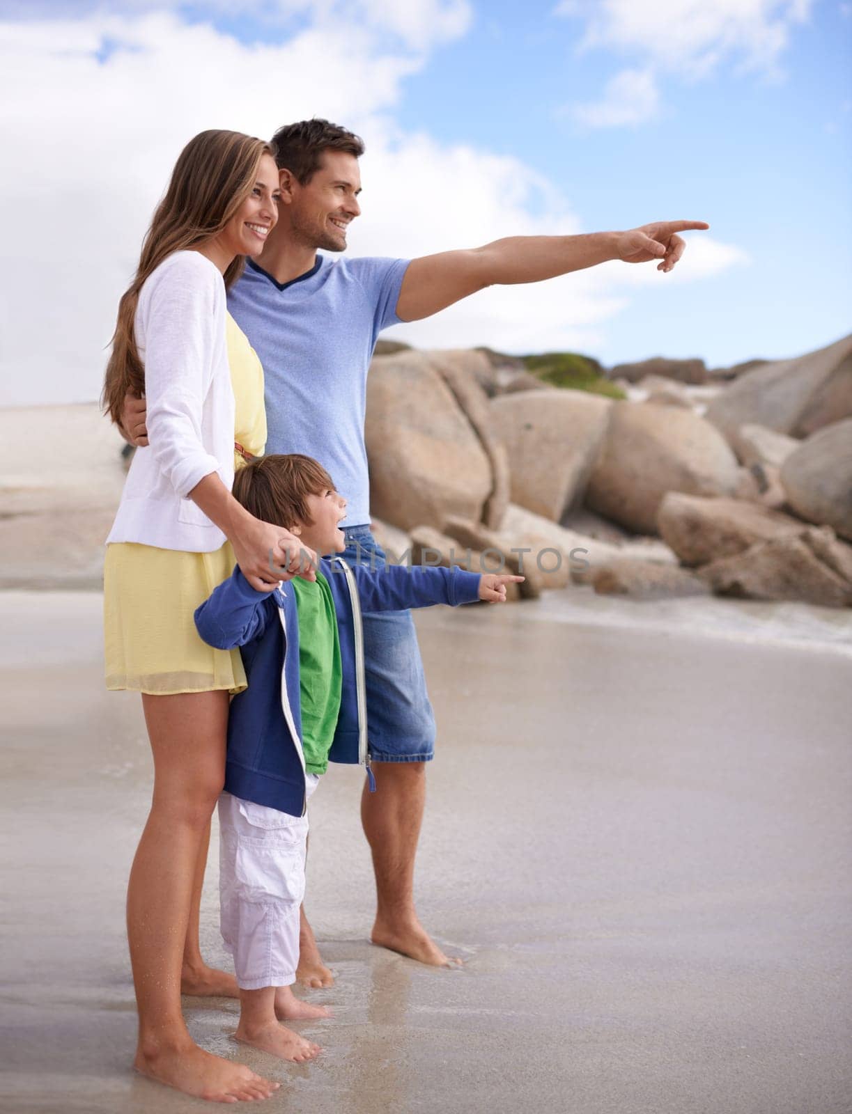 Family, child and pointing outdoor at beach for travel, adventure or holiday in summer with a smile. A man, woman and kid or son together on vacation at sea for blue sky, learning and happiness.