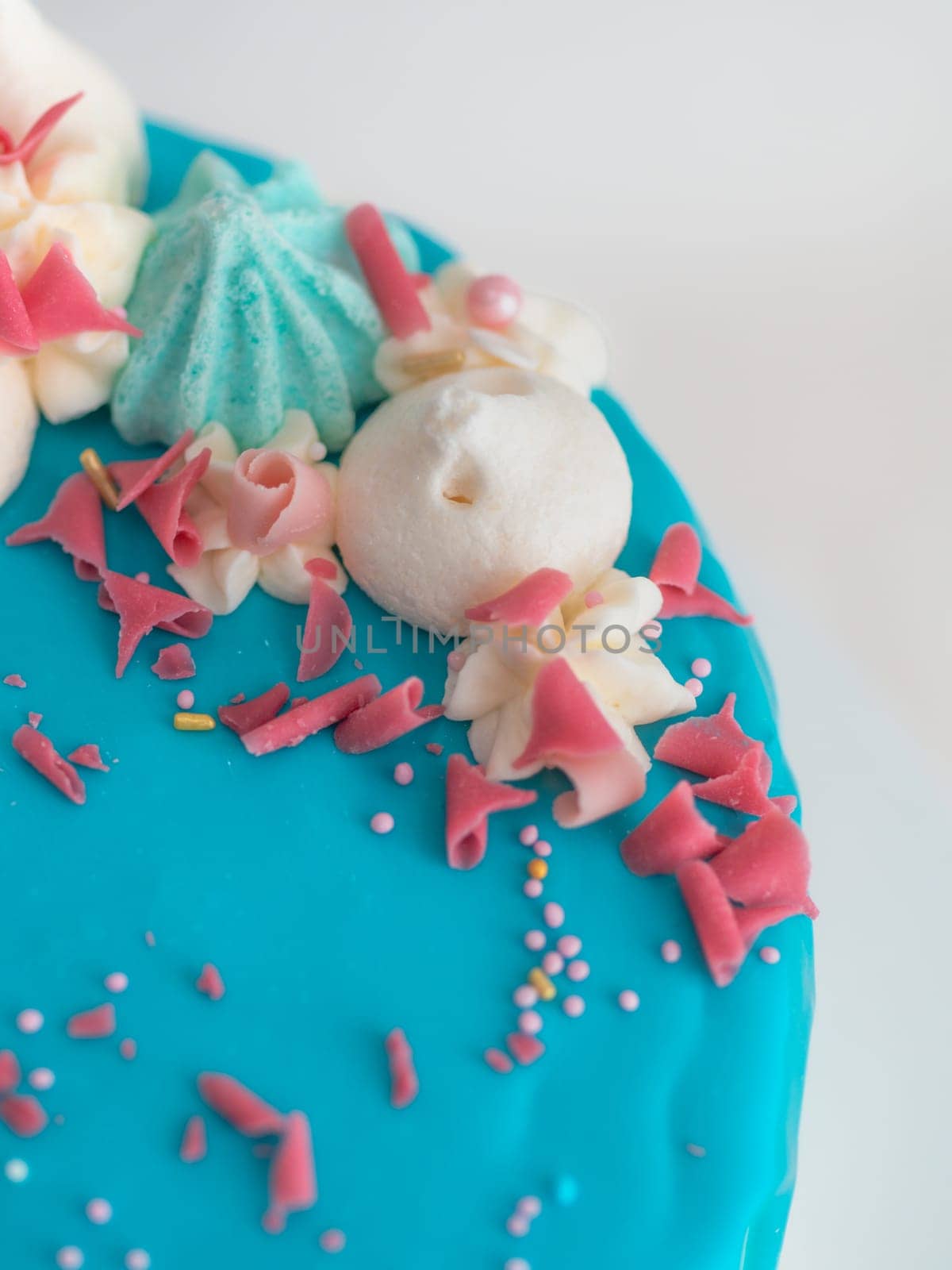 studio shot of chocolate frosted blue dripped icing white cup cake, unicorn , meringue and sprinkles on top