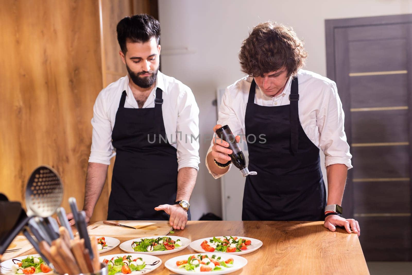 Chef pouring dressing over caprese salad in restaurant kitchen - food concept