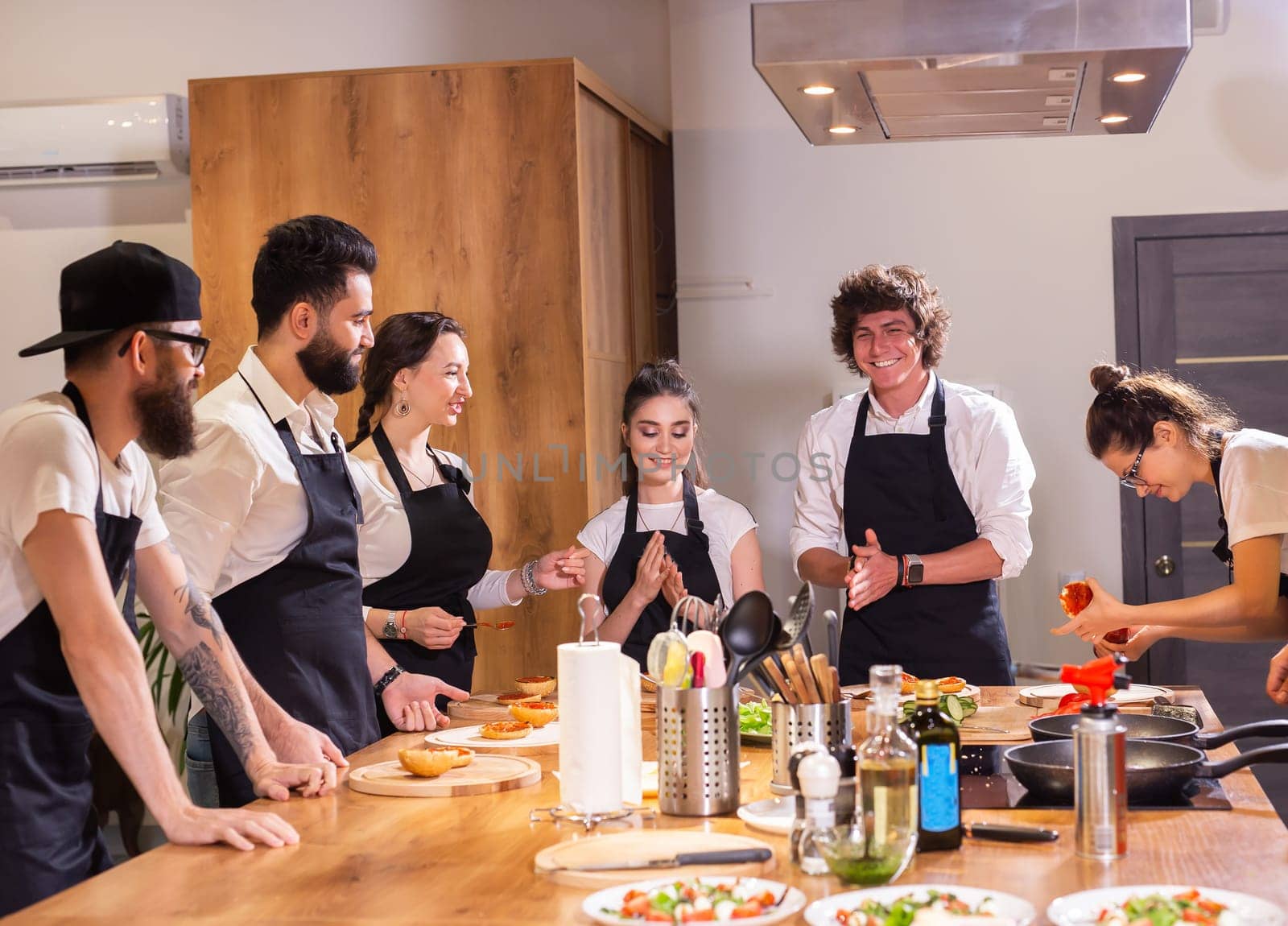 Cooking course concept - senior male chef in cook uniform teaches young people cooking class students to prepare and mix ingredients for dishes in restaurant kitchen