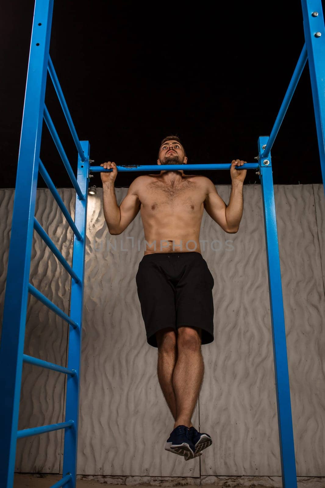 Strong young athlete is engaged in on sports field. Athletic man. Exercises on uneven bars. Athlete Outdoors.