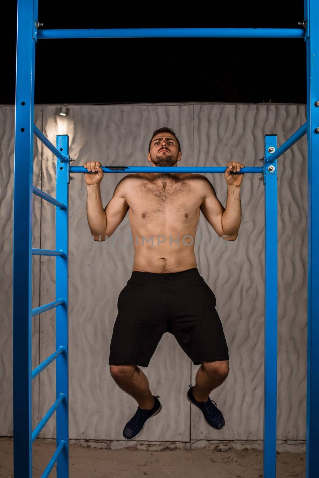Strong young athlete is engaged in on sports field. Athletic man. Exercises on uneven bars. Athlete Outdoors.