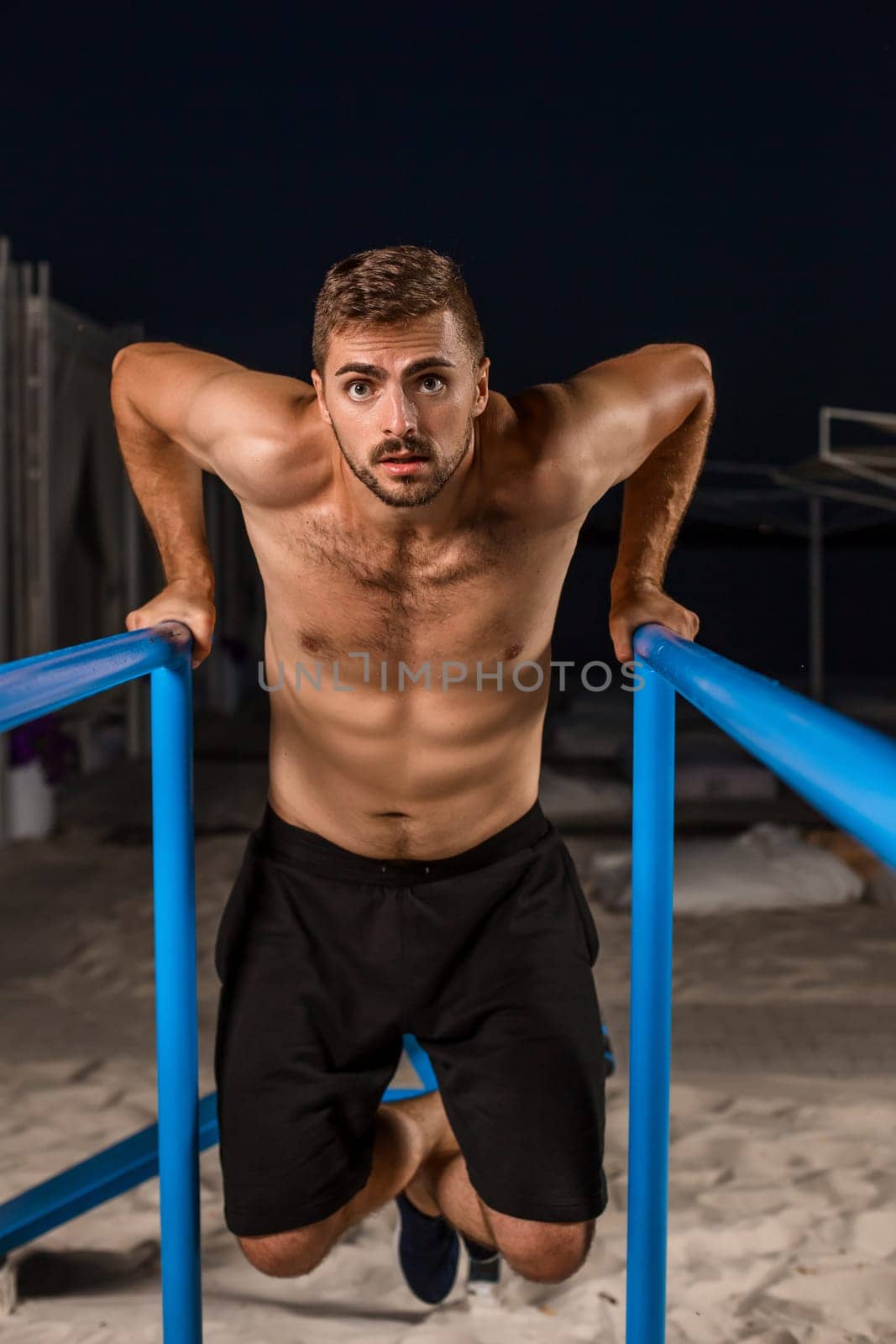 Strong young athlete is engaged in on sports field. Athletic man. Exercises on uneven bars. Athlete Outdoors.
