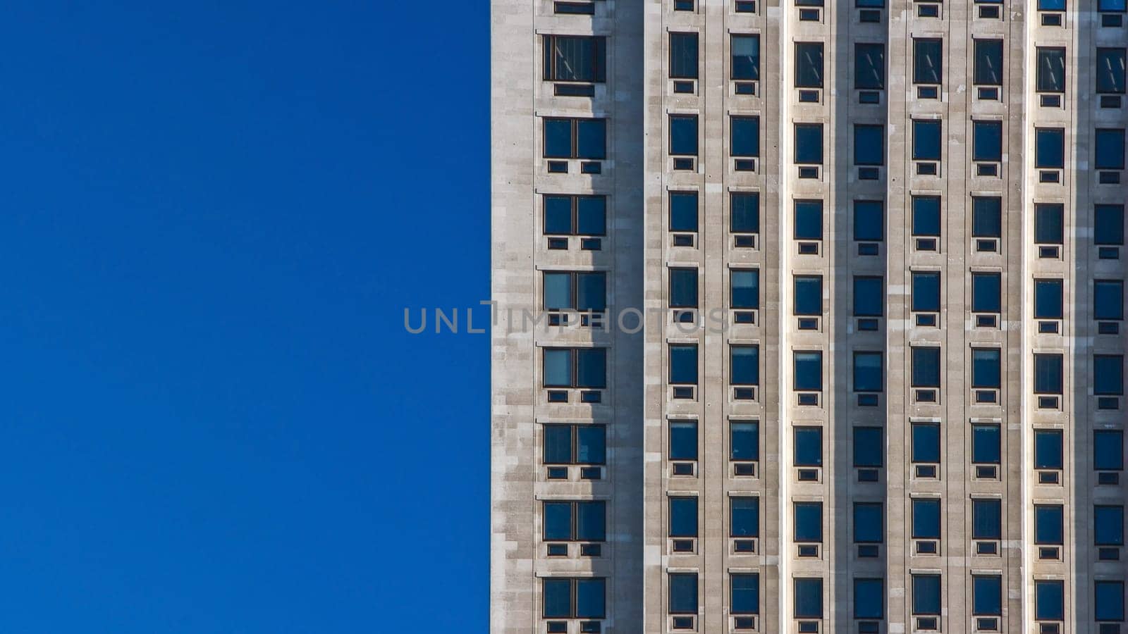 Regular pattern made of rectangular windows on block of flats / offices building. Clear sky (place for text) on left side.