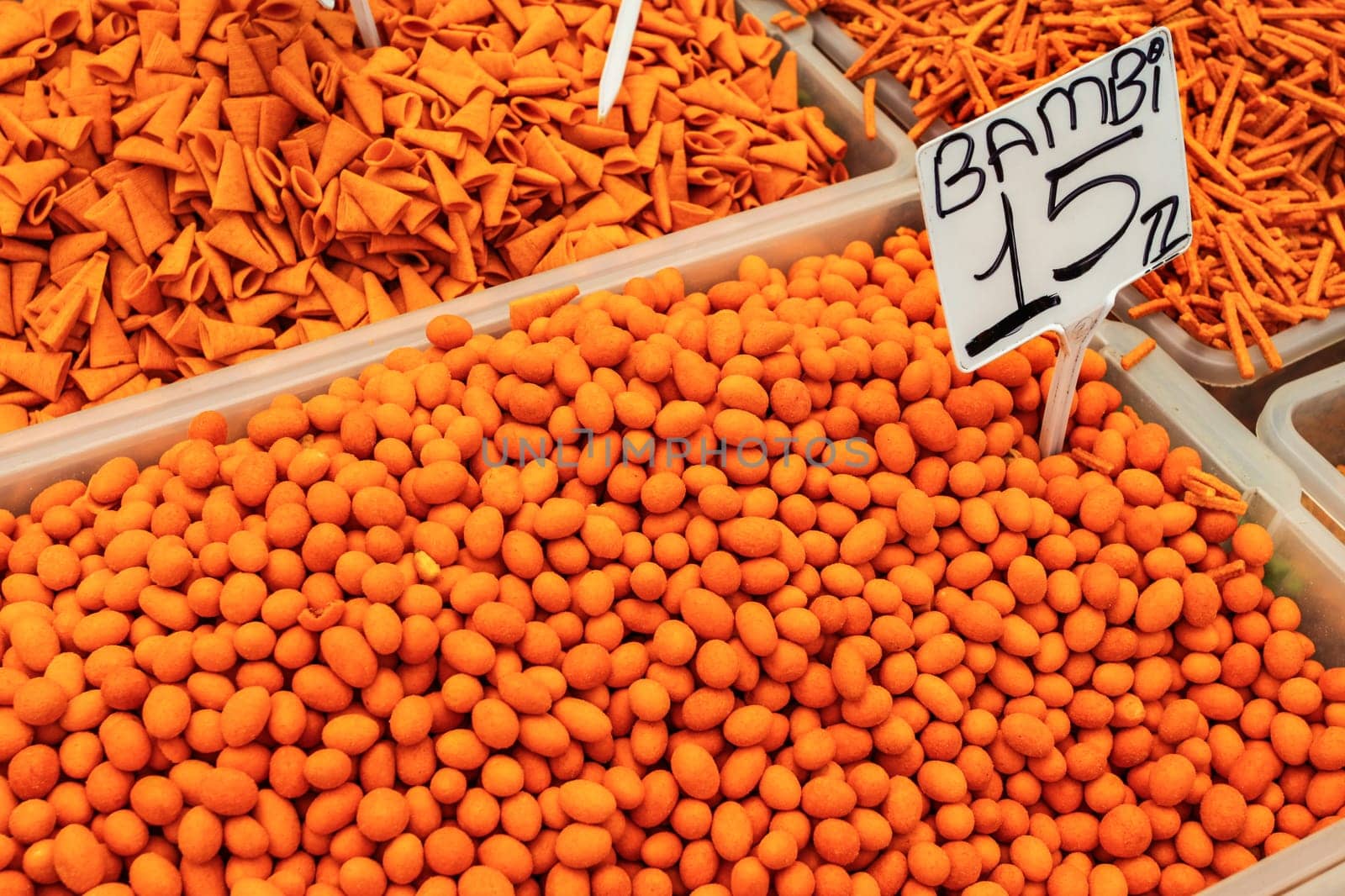 Orange (from paprika) spiced nuts and crackers displayed on food market. "Bambi" variety label with price tag in Turkish liras.