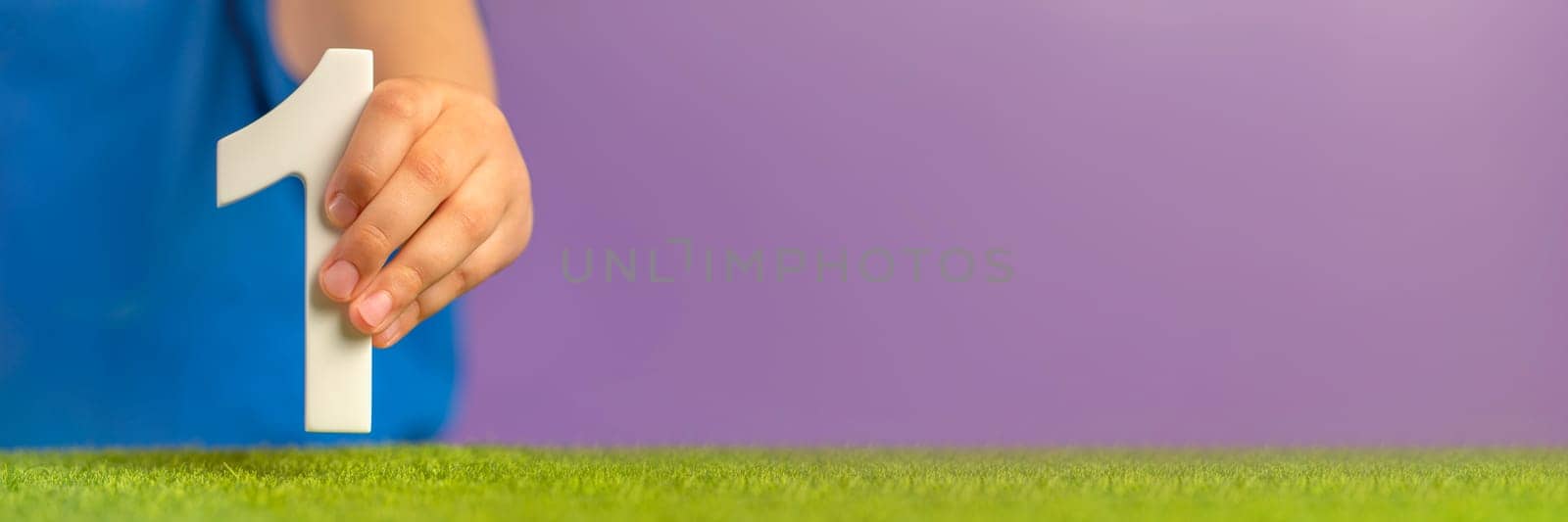 Banner with hand holding number one on green grass and purple background. A symbol of unity, uniqueness and beginning, joining forces to achieve a common goal, the first step in a certain direction. by SERSOL