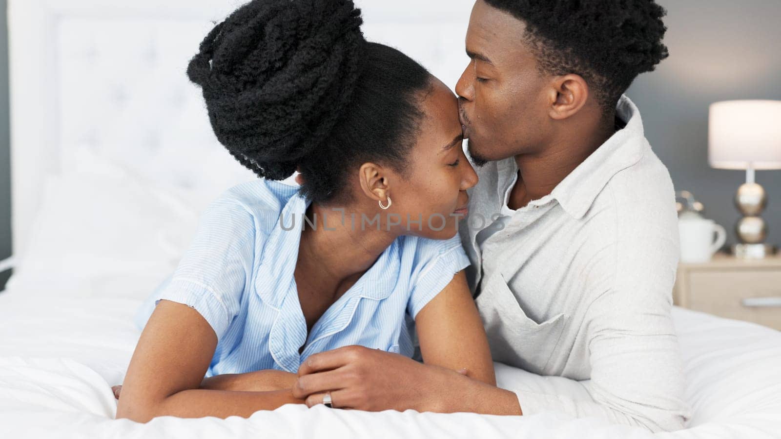 Love, support and trust between black couple sharing a special bond and communication while spending time in the bedroom. Commitment, marriage and understanding with man kissing head of woman by YuriArcurs