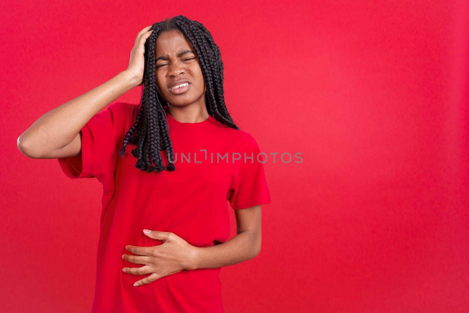 African woman gesturing bodily discomfort and headache in studio with red background