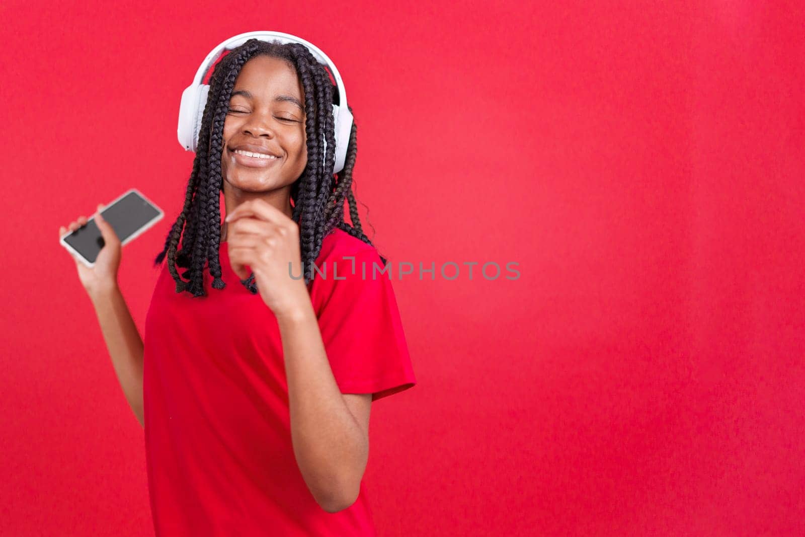 African woman listening to music dancing with the eyes closed in studio with red background