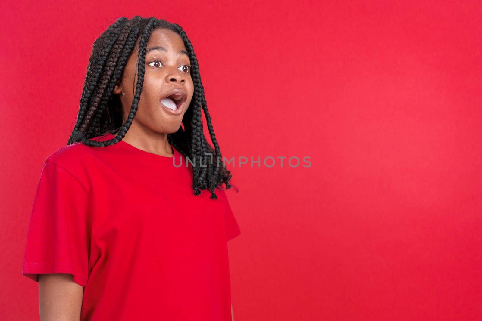 Surprised african woman open the mouth and looking away in studio with red background