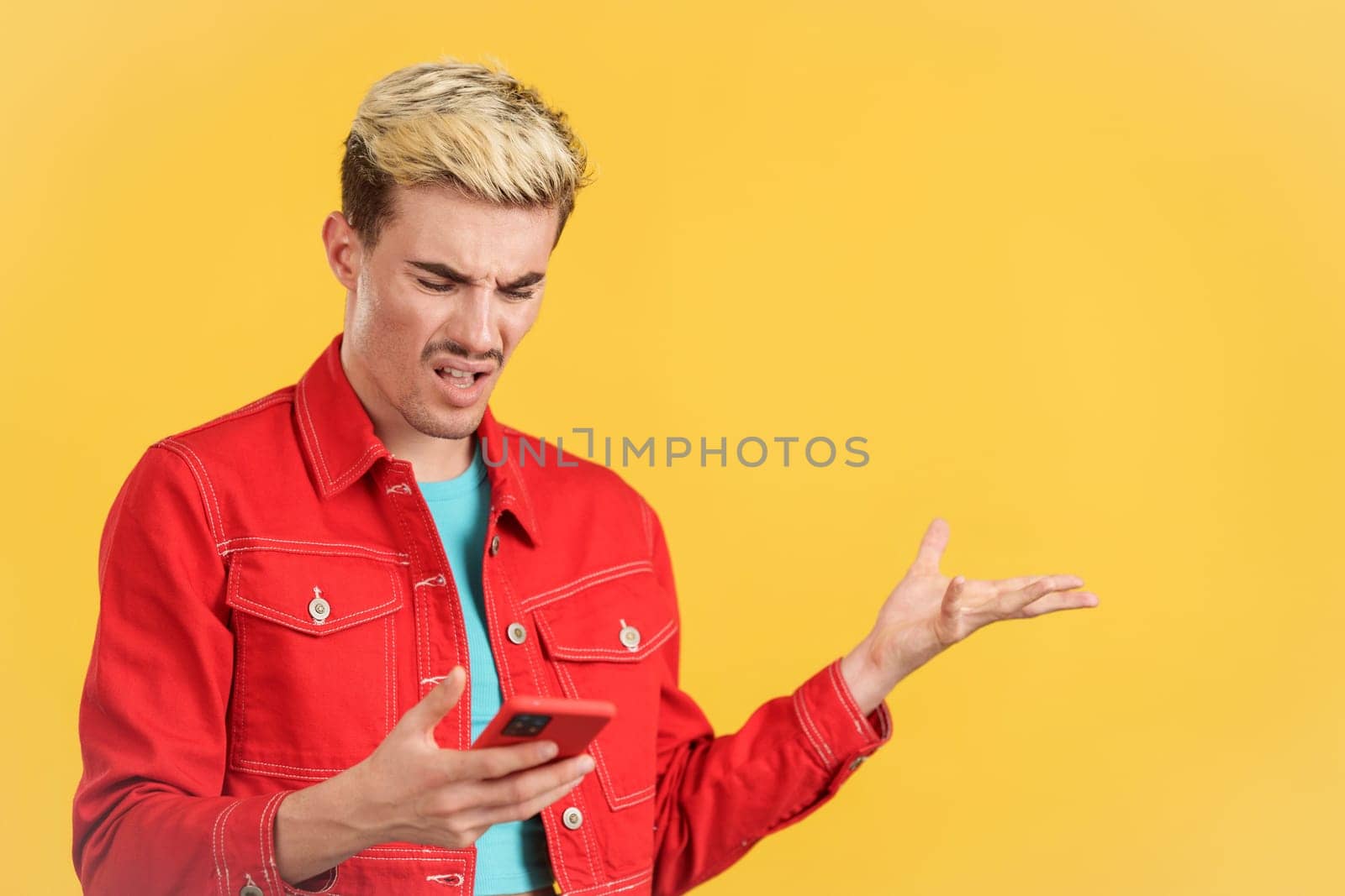 Worried gay man using a mobile phone in studio with yellow background