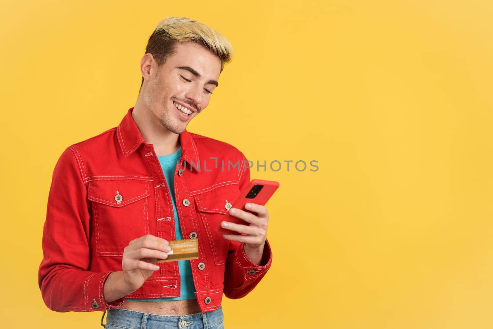 Happy gay man using the mobile and card to shopping online in studio with yellow background