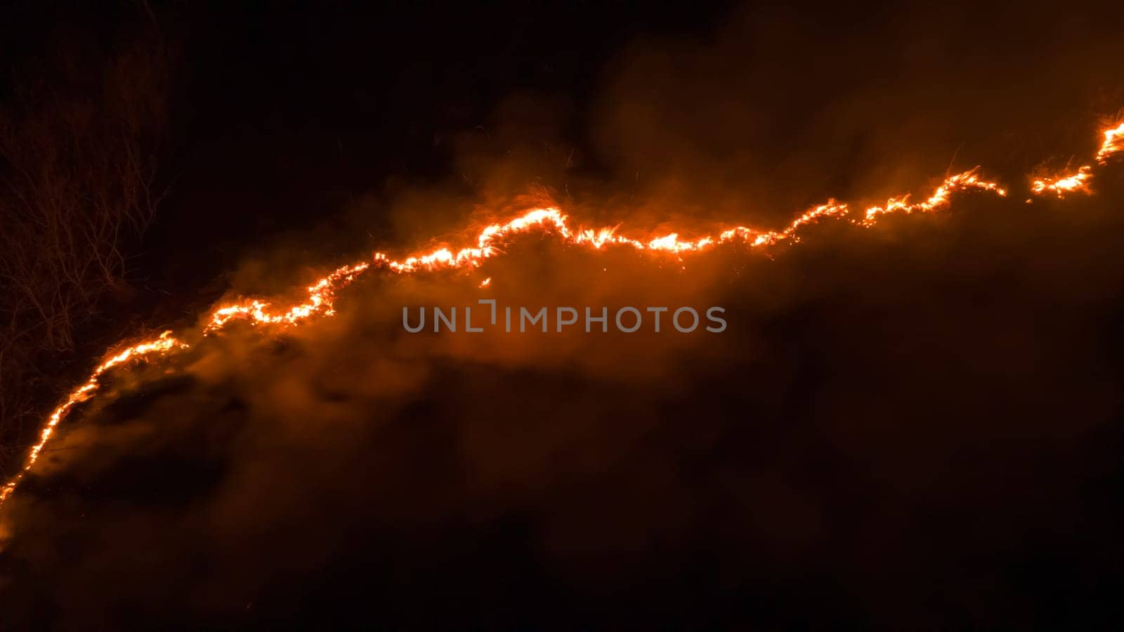 Night fire in the forest with fire and smoke.Epic aerial photo of a smoking wild flame.A blazing,glowing fire at night.Forest fires.Dry grass is burning. climate change,ecology.Line fire in the dark.