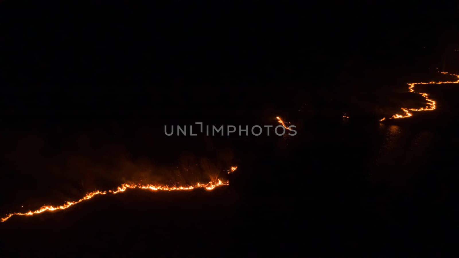 Night fire in the forest with fire and smoke.Epic aerial photo of a smoking wild flame.A blazing,glowing fire at night.Forest fires.Dry grass is burning. climate change,ecology.Line fire in the dark.