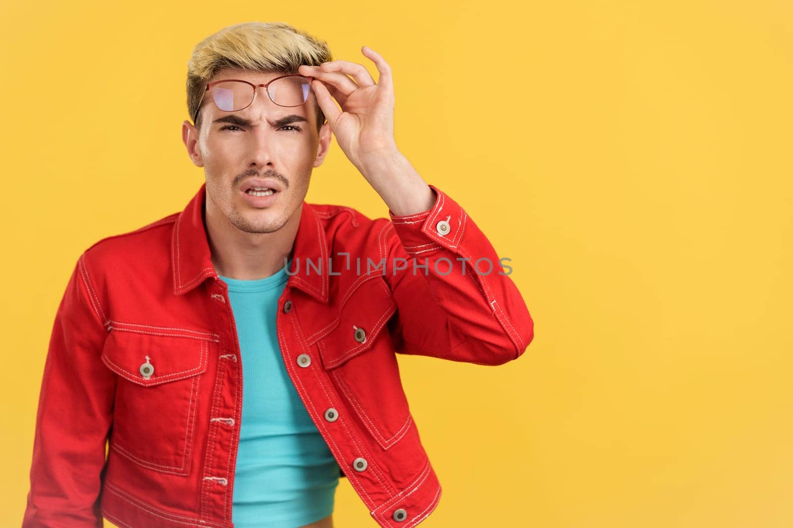 Gay man taking off the glasses to see far away in studio with yellow background