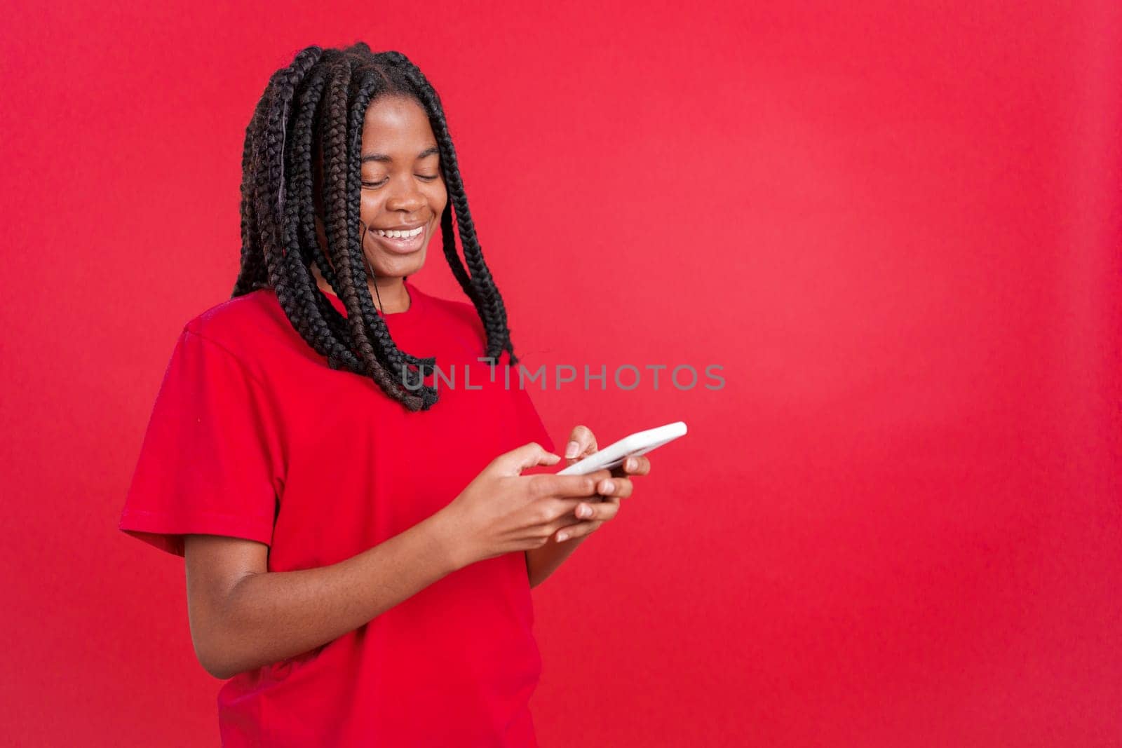 Happy african woman smiling while using the mobile in studio with red background