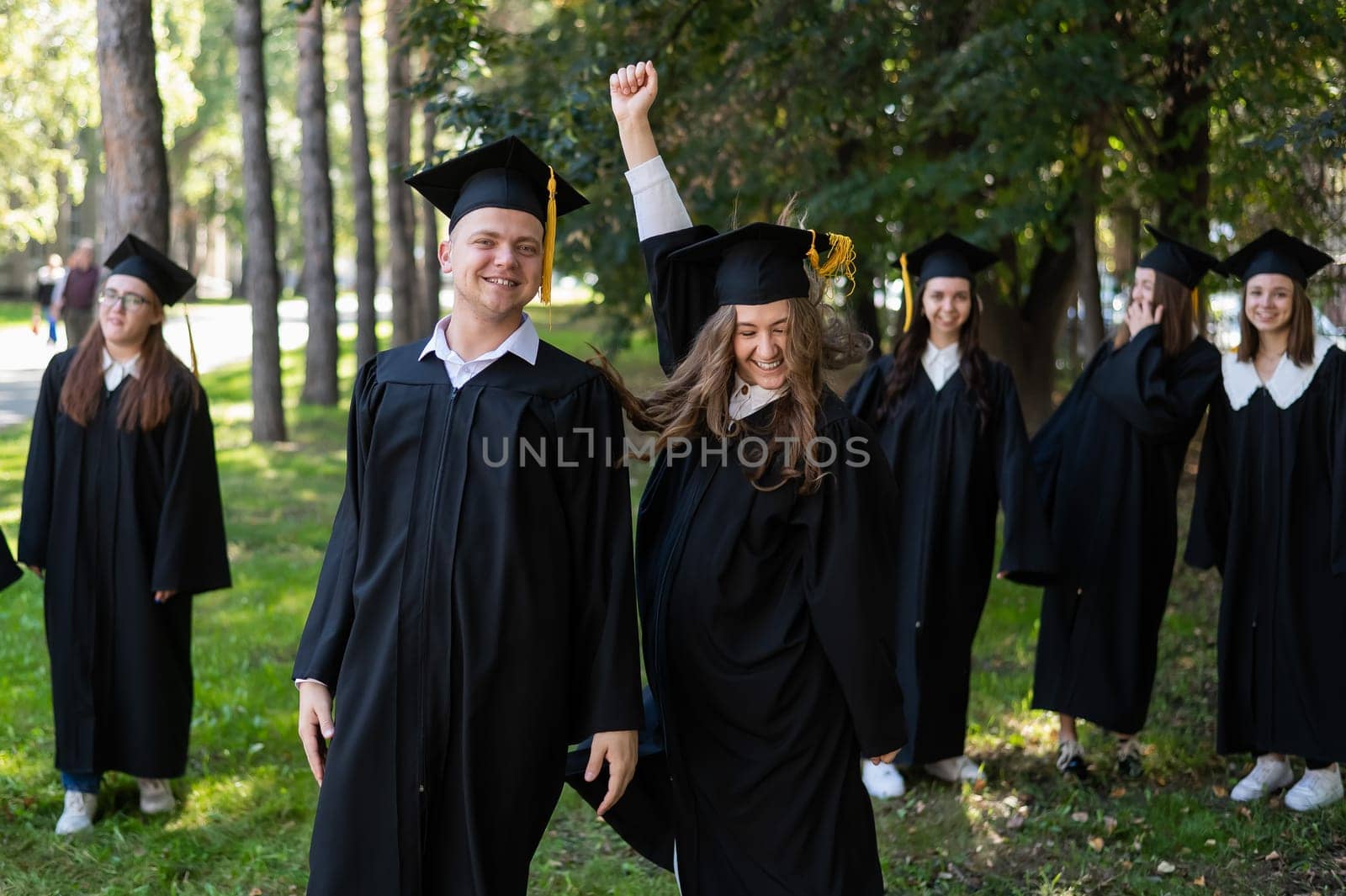 Group of happy young people in graduation gowns outdoors. Students are walking in the park