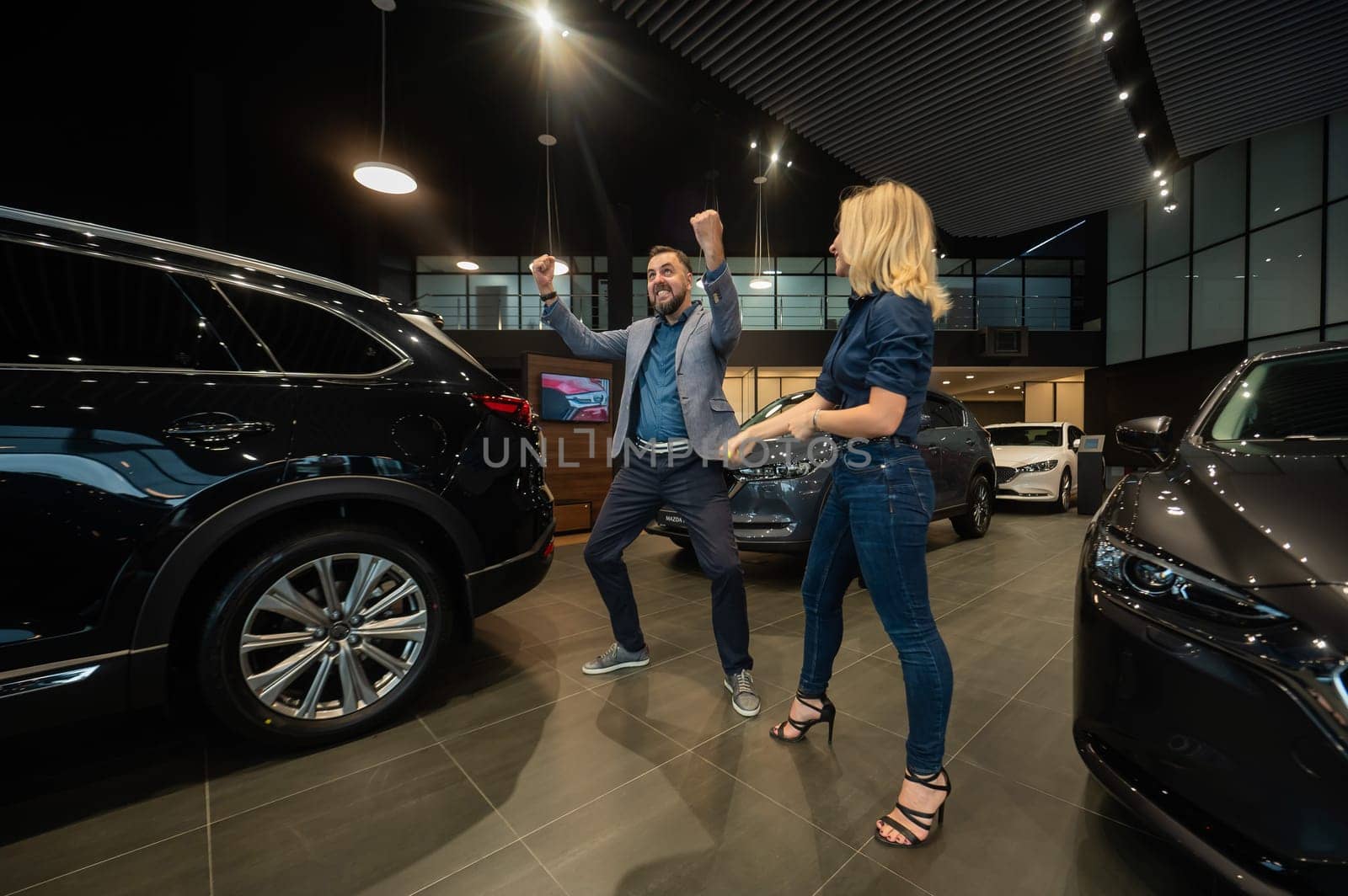 Happy married couple celebrating buying a car in a car showroom