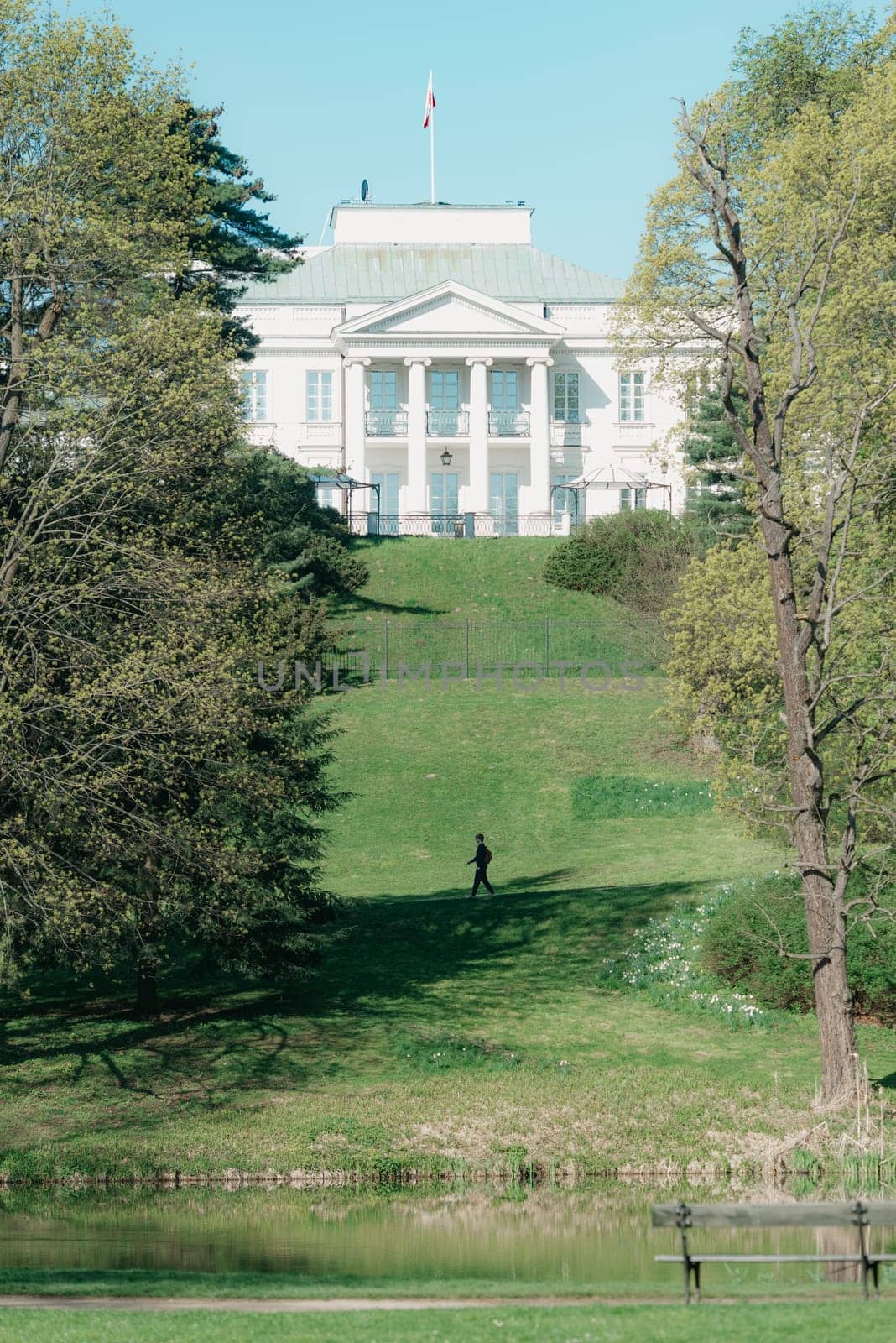 The classical white building on the hill in the center of the park in the spring. Classicism in the architecture of the government building above the lake in the morning.
