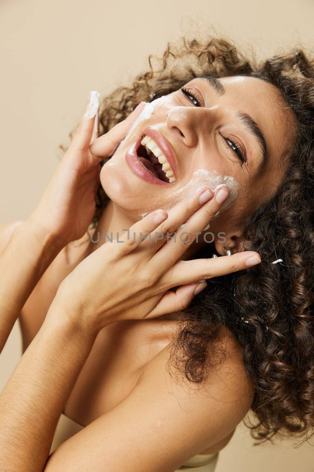 Woman beauty face close-up applying foam to wash and cleanse skin with fingers of her hand, nail and hair health, hair dryer style curly afro hair, body and beauty care concept by SHOTPRIME