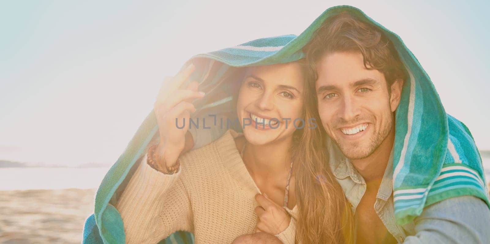 Getting close at the beach. A blissful couple covering their heads with a towel while enjoying a day at the beach