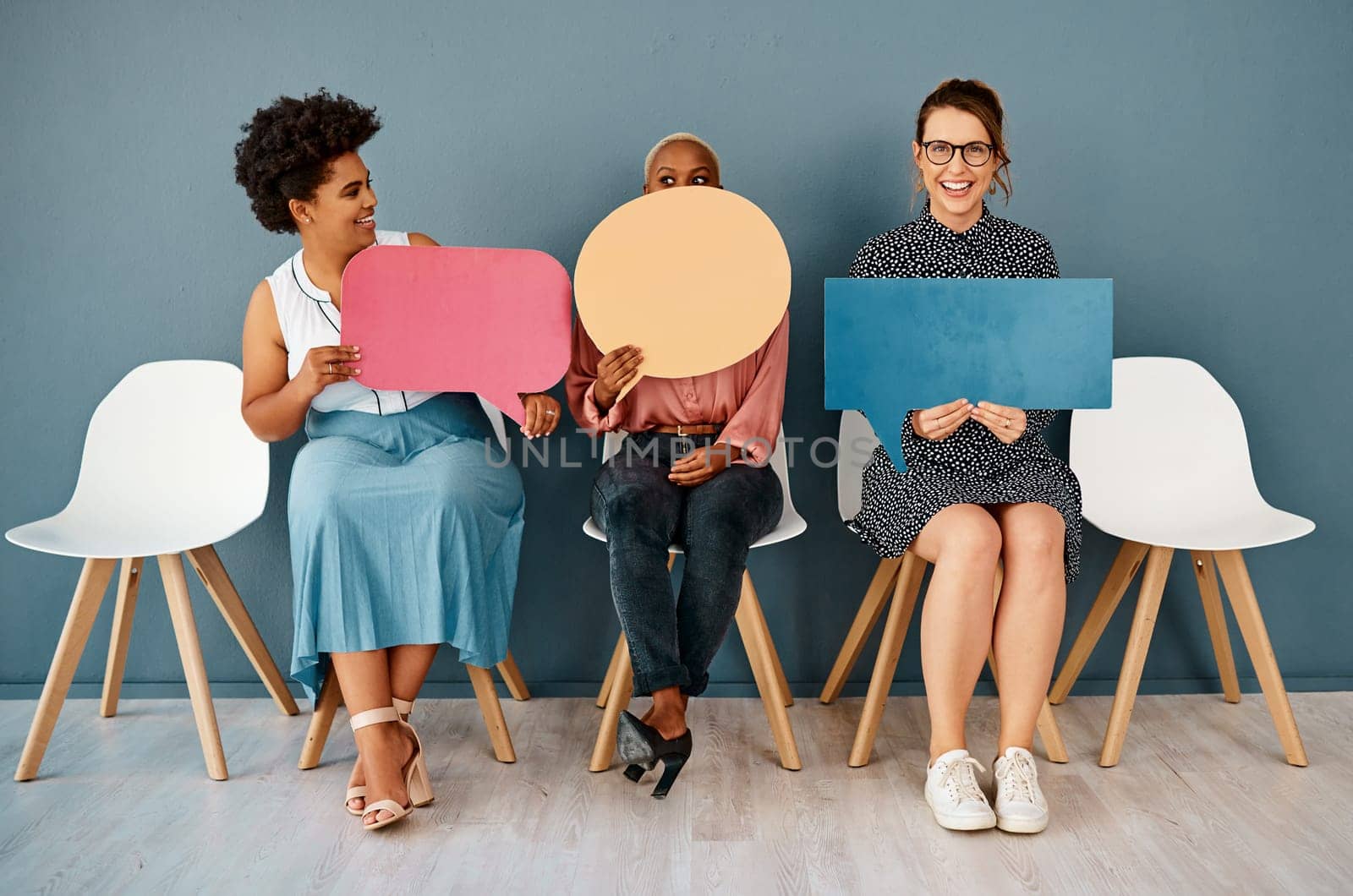 Okay guys forget I said that. Studio shot of a group of attractive young businesswomen holding speech bubbles while sitting in a row against a grey background