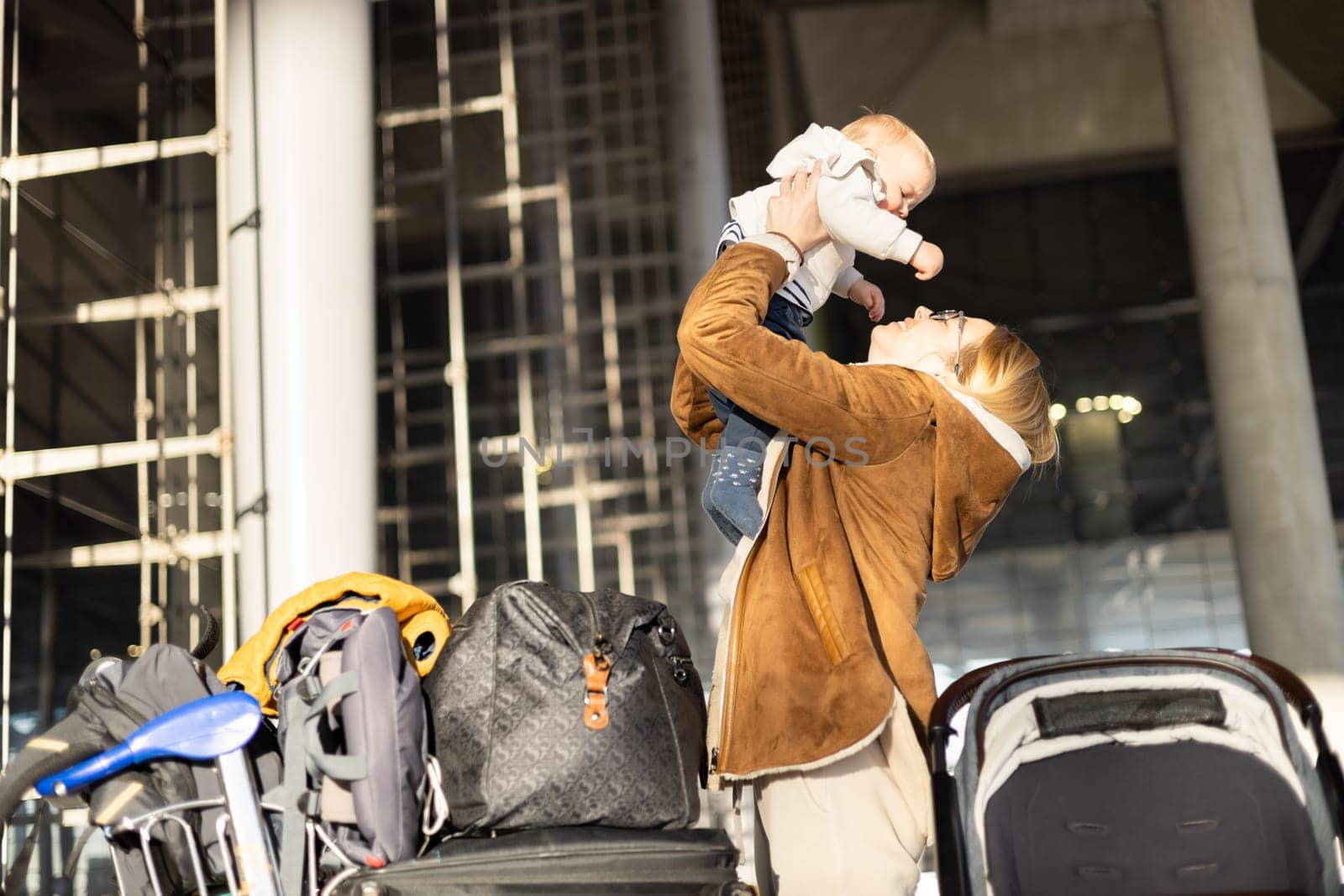Motherat happily holding and lifting his infant baby boy child in the air after being rejunited in front of airport terminal station. Baby travel concept. by kasto