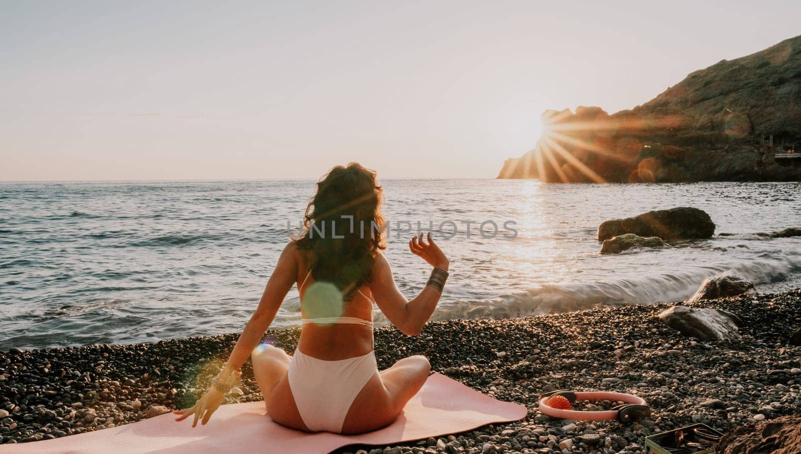 Woman sea yoga. Happy woman in white swimsuit and boho style braclets practicing outdoors on yoga mat by sea on sunset. Women yoga fitness routine. Healthy lifestyle, harmony and meditation by panophotograph