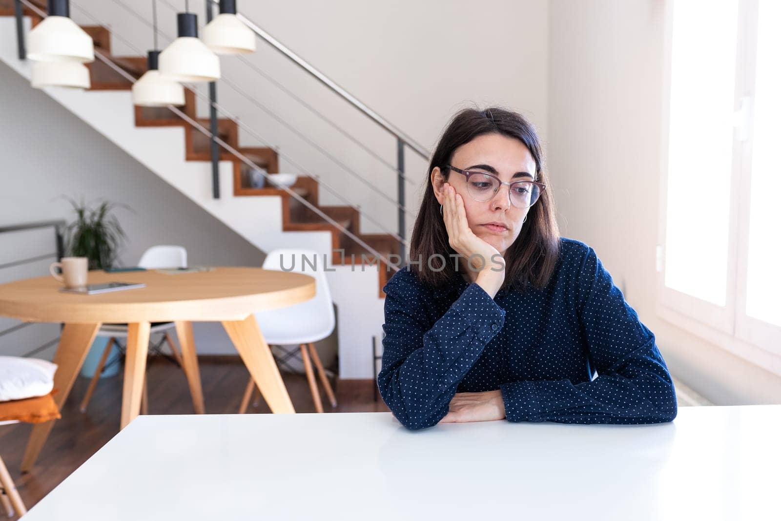 Pensive young caucasian woman with glasses feeling bored sitting at home office desk. Lifestyle concept.