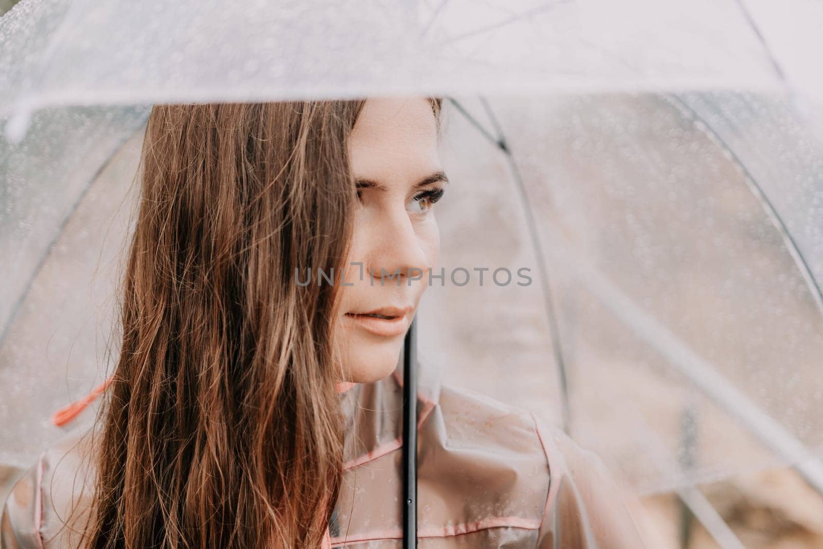 Woman rain umbrella. Happy woman portrait wearing a raincoat with transparent umbrella outdoors on rainy day in park near sea. Girl on the nature on rainy overcast day. by panophotograph