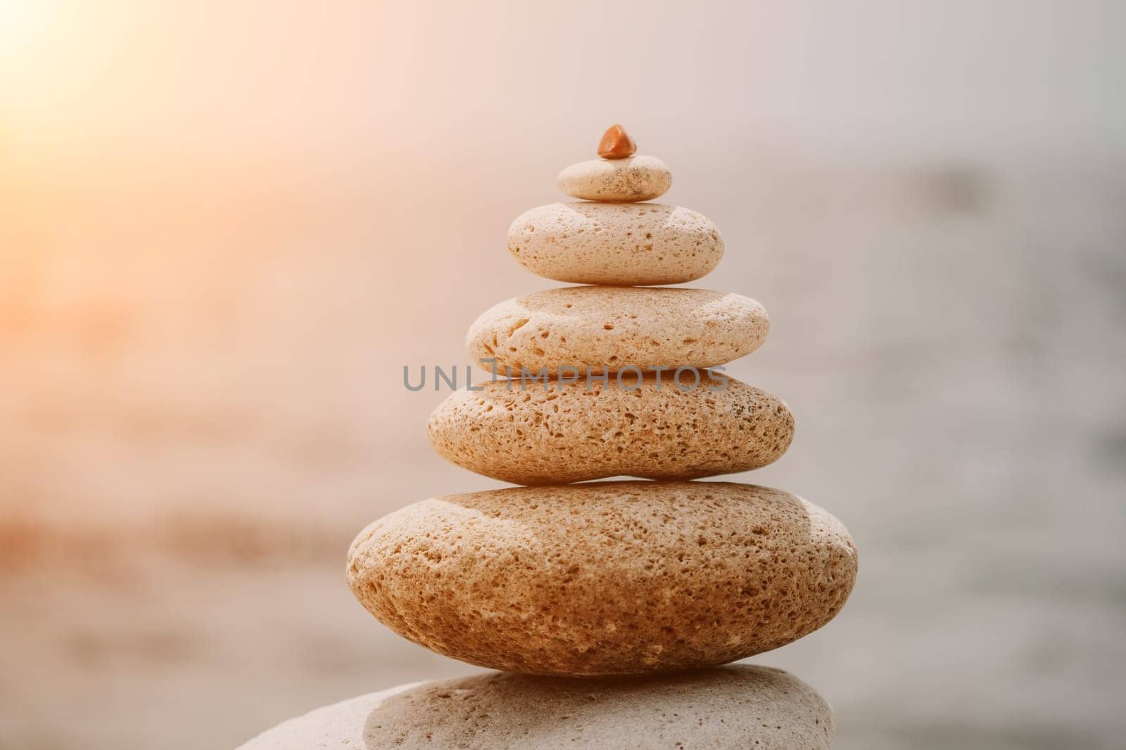 Pyramid stones on the seashore with warm sunset on the sea background. Happy holidays. Pebble beach, calm sea, travel destination. Concept of happy vacation on the sea, meditation, spa, calmness.