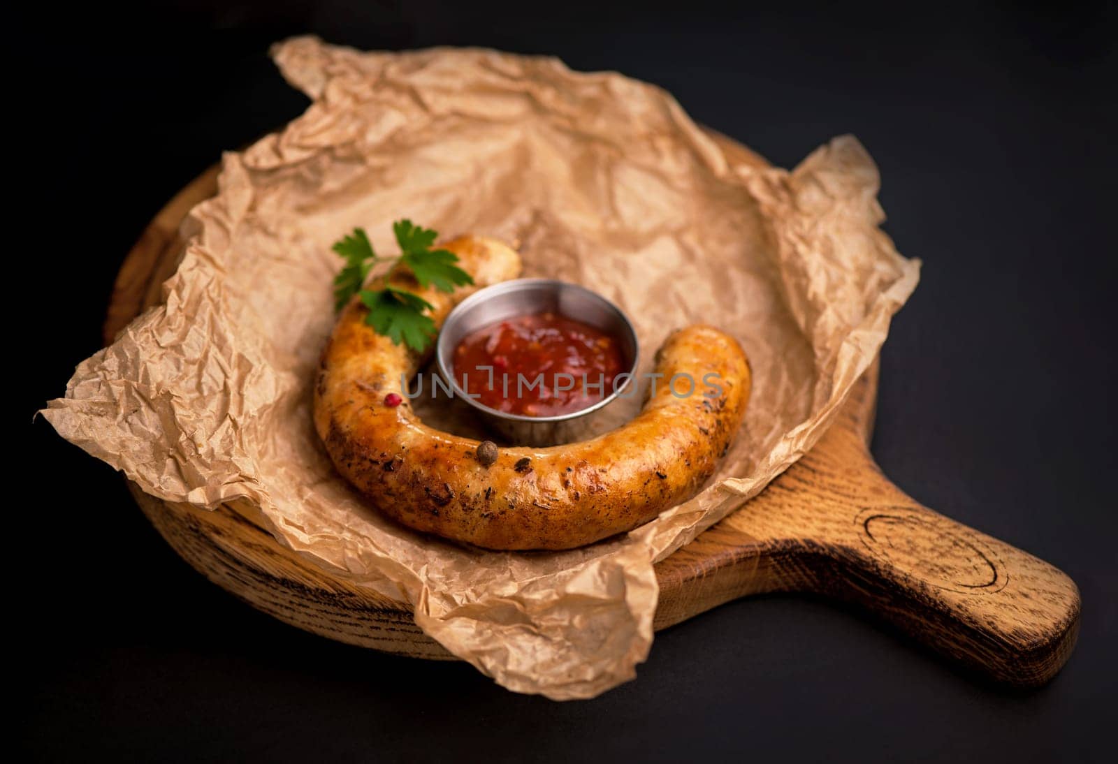 grilled sausages with sauce on a wooden board on a black background