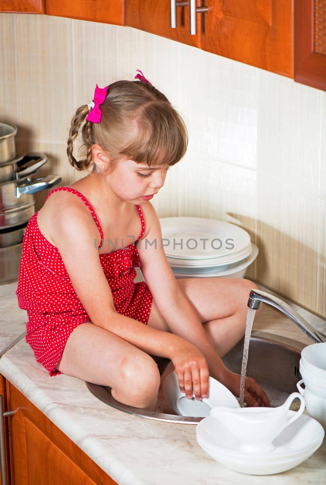 The concept of mother's helper, child development, family. Little girl washes white dishes at home in the kitchen by aprilphoto
