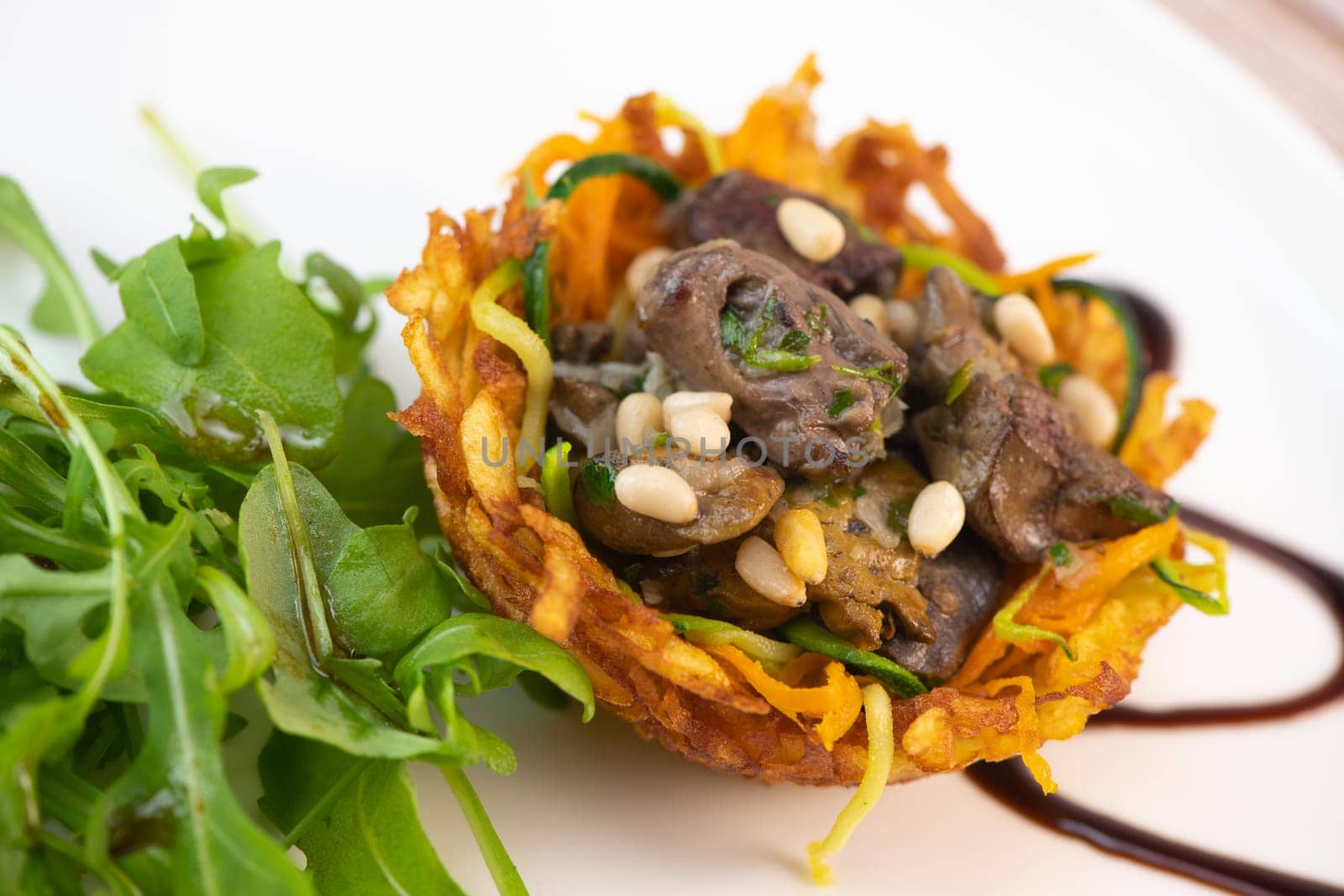 Recipe for poultry giblets in a nest of fried potatoes with rocket and tomato salad. High quality photo