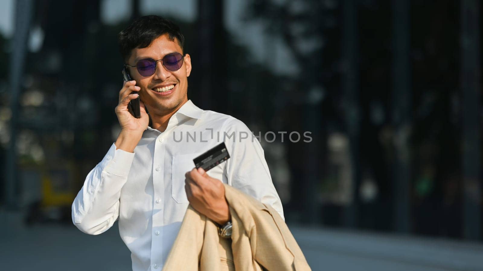 Smiling businessman utalking on mobile phone while walking in business district. Modern lifestyle, technology and business concept.