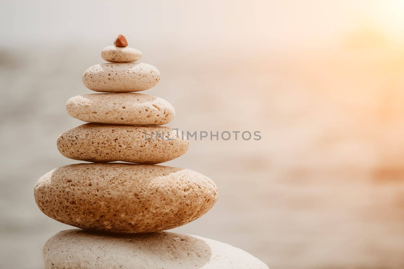 Pyramid stones on the seashore with warm sunset on the sea background. Happy holidays. Pebble beach, calm sea, travel destination. Concept of happy vacation on the sea, meditation, spa, calmness.